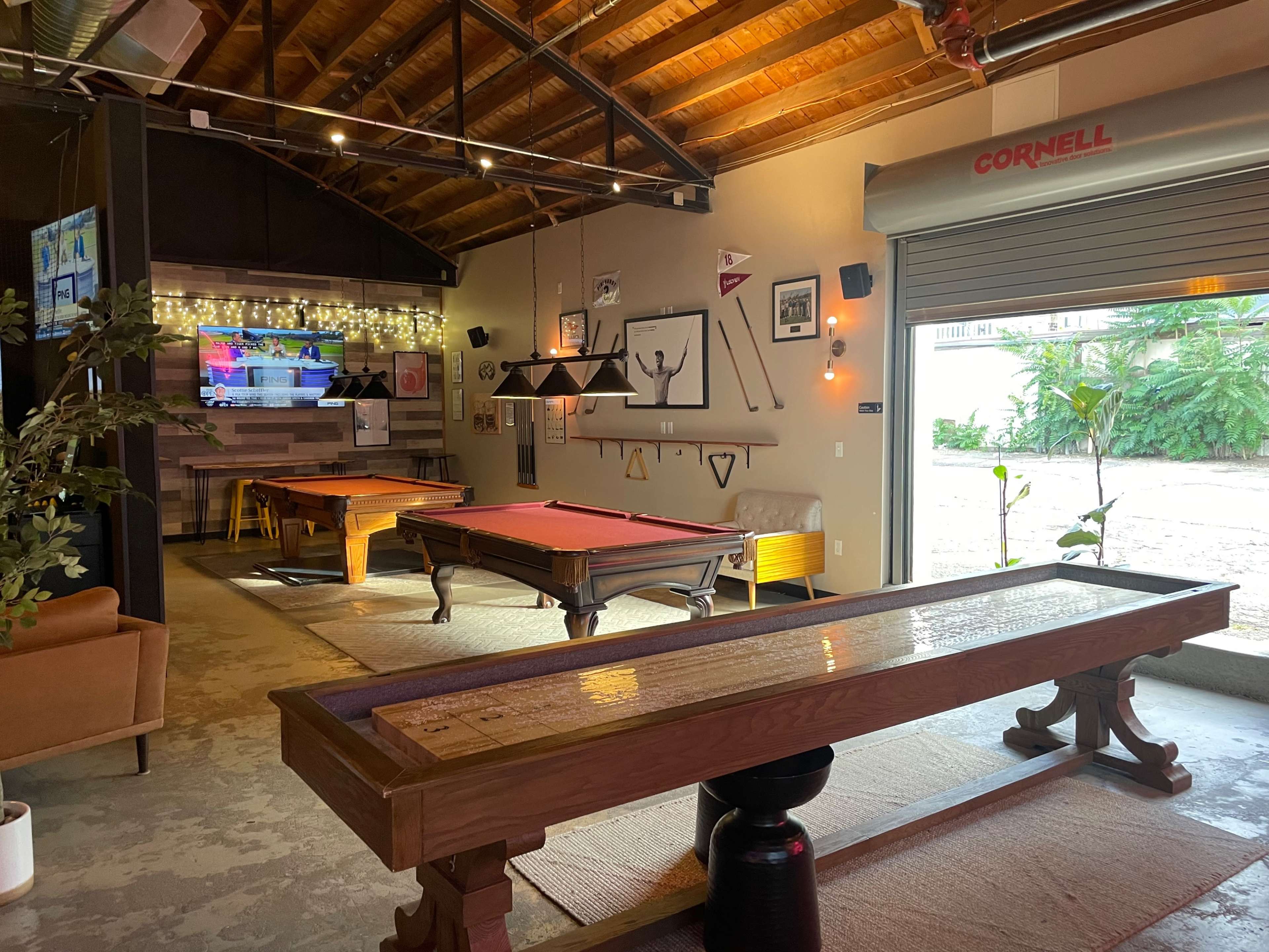 A recreational room featuring a billiards table, a shuffleboard table, and a television against a backdrop of wood beams and wall decor.
