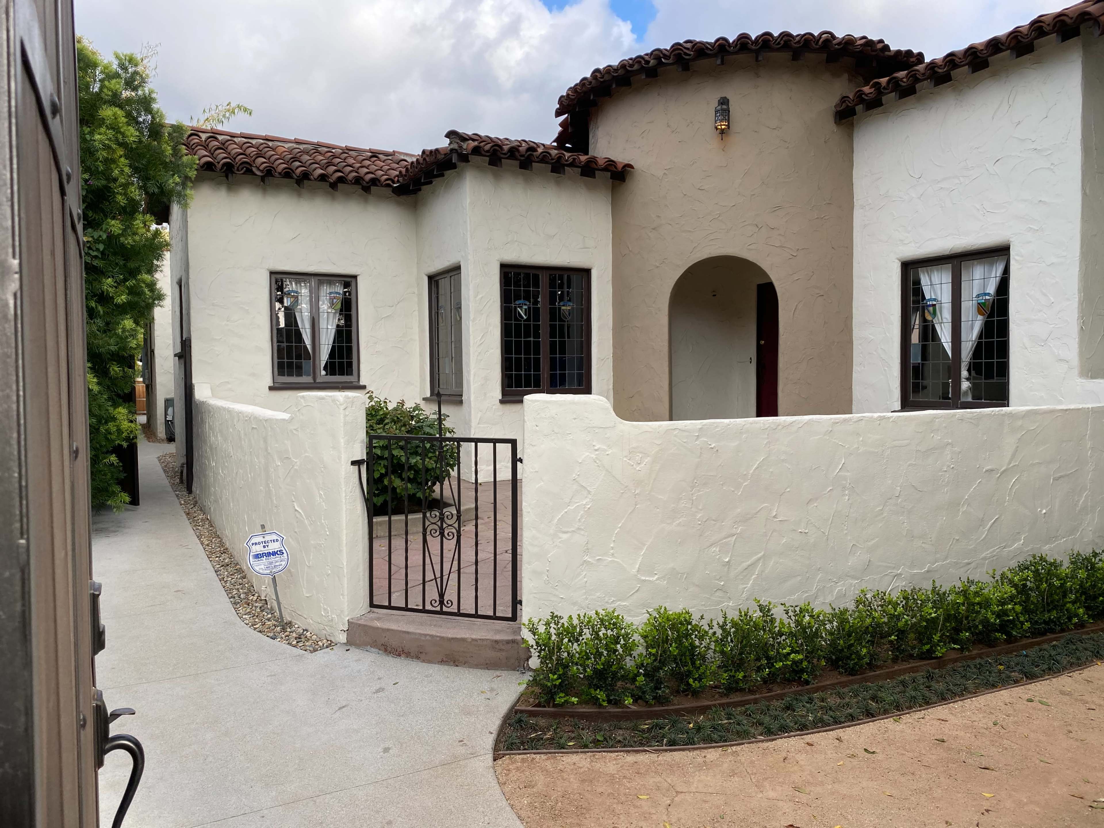 A single-story house with a stucco exterior, a tiled roof, and a gated entryway leading to a small front patio.