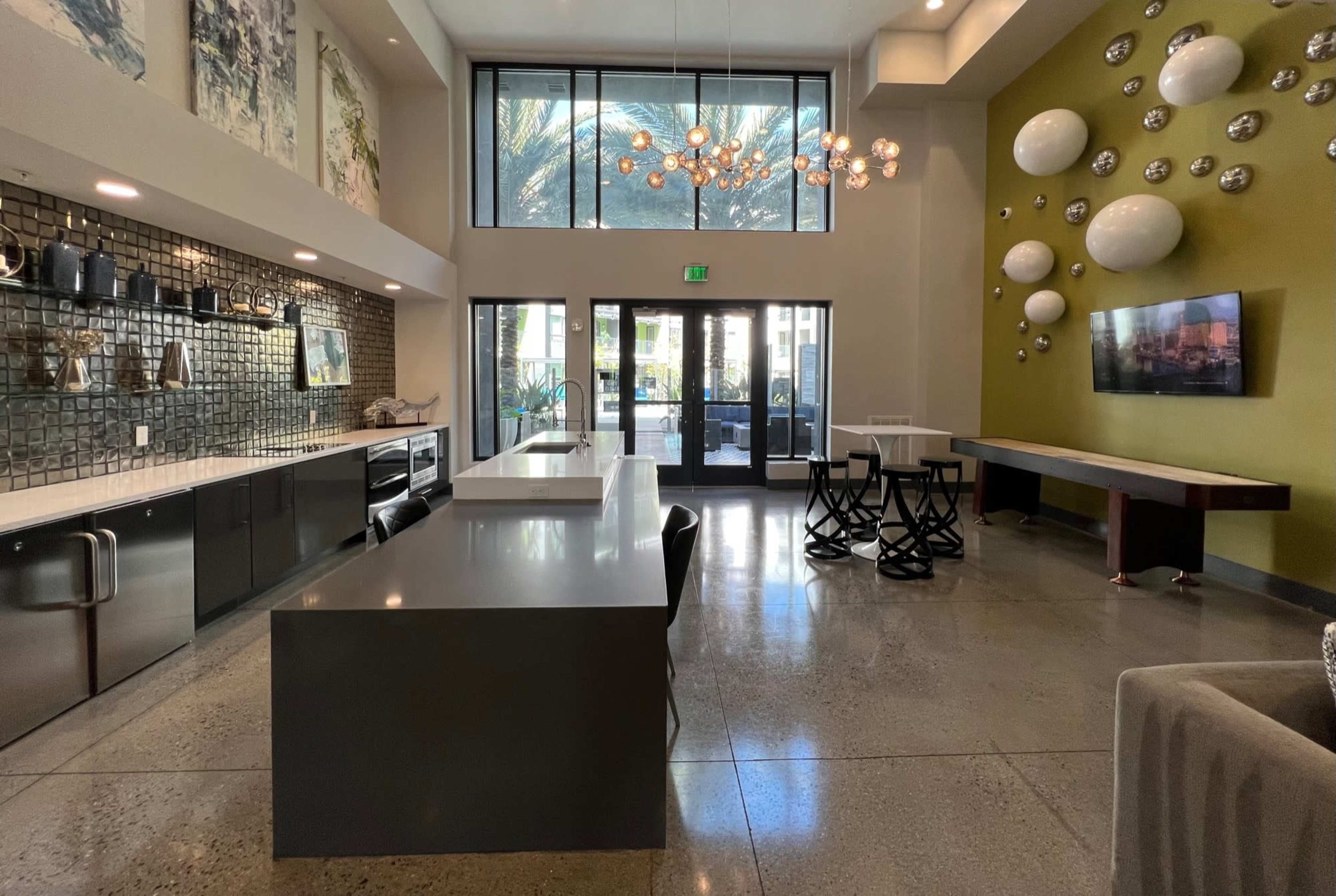 A modern common area with a kitchen island, sleek black cabinets, and large windows overlooking a patio.