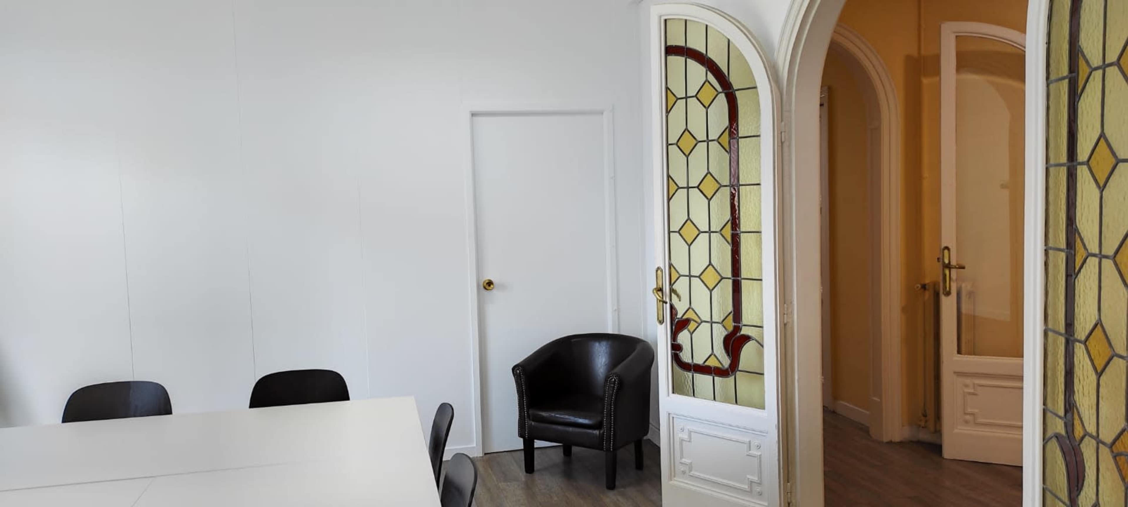 The image shows a minimalistic meeting room with a white table, black chairs, and an arched doorway leading to a hallway with a decorative glass panel.