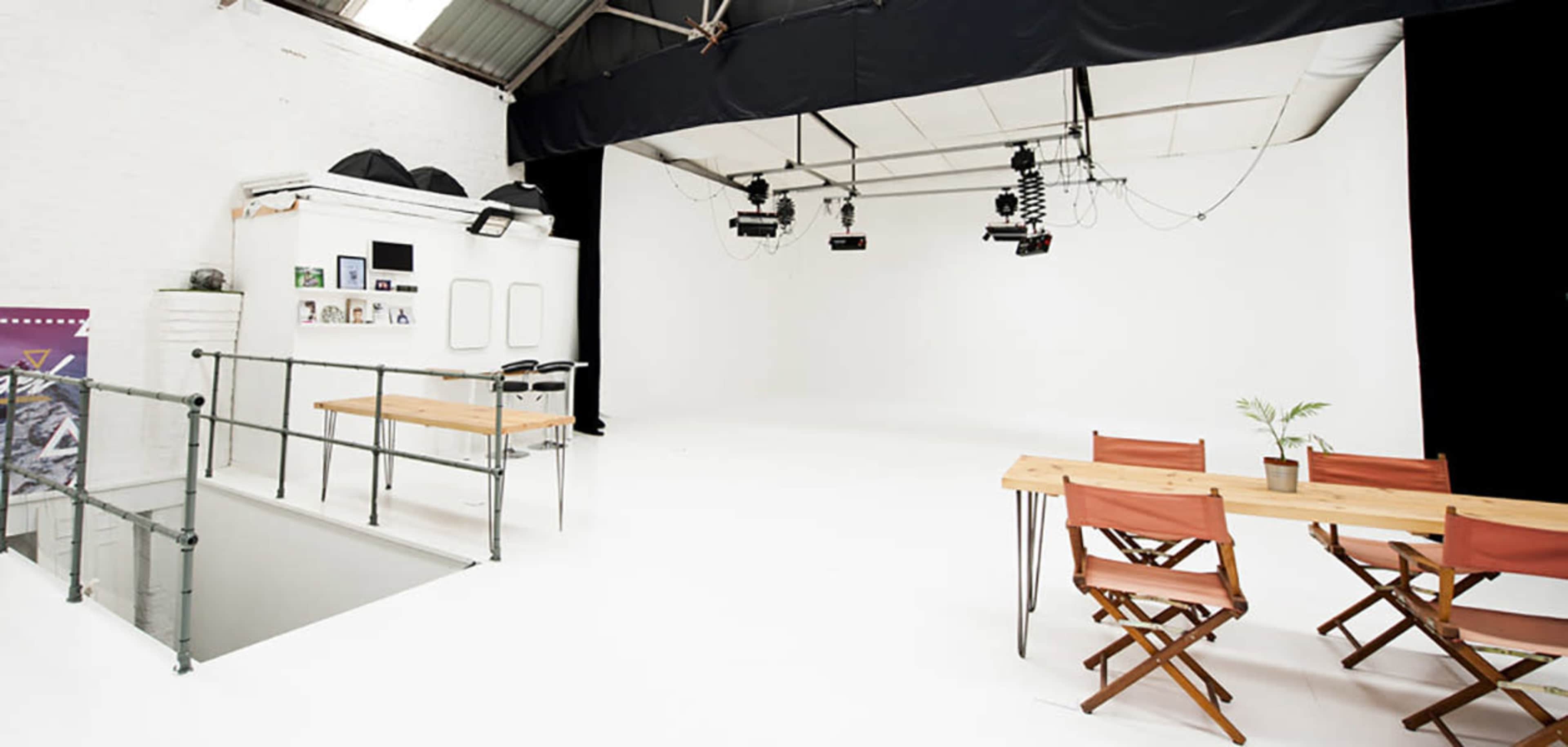 A spacious, minimally decorated studio with white walls, a clean floor, and a wooden table set with chairs.
