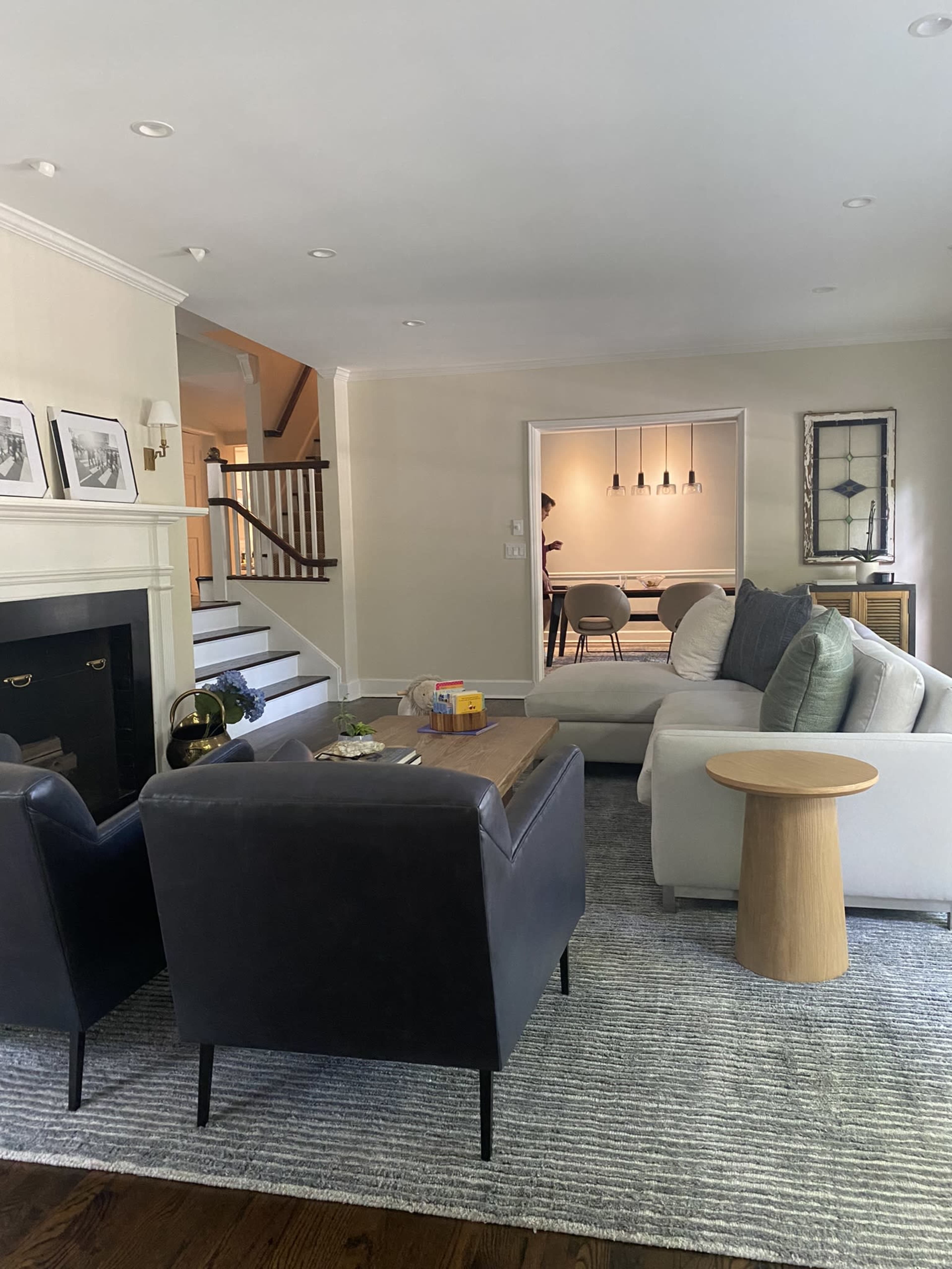 A cozy living room with a black leather chair, a light-colored sofa, a wooden coffee table, and a view of a dining area through an open doorway.