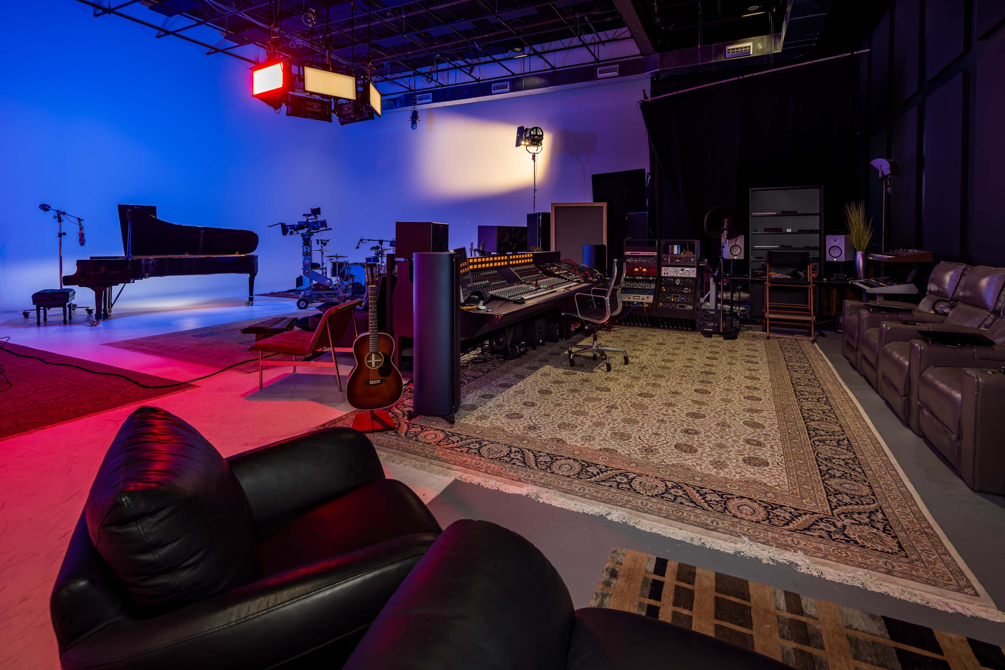 The image shows a music studio with a grand piano, recording equipment, and a comfortable seating area, all set against a backdrop of colored lighting.