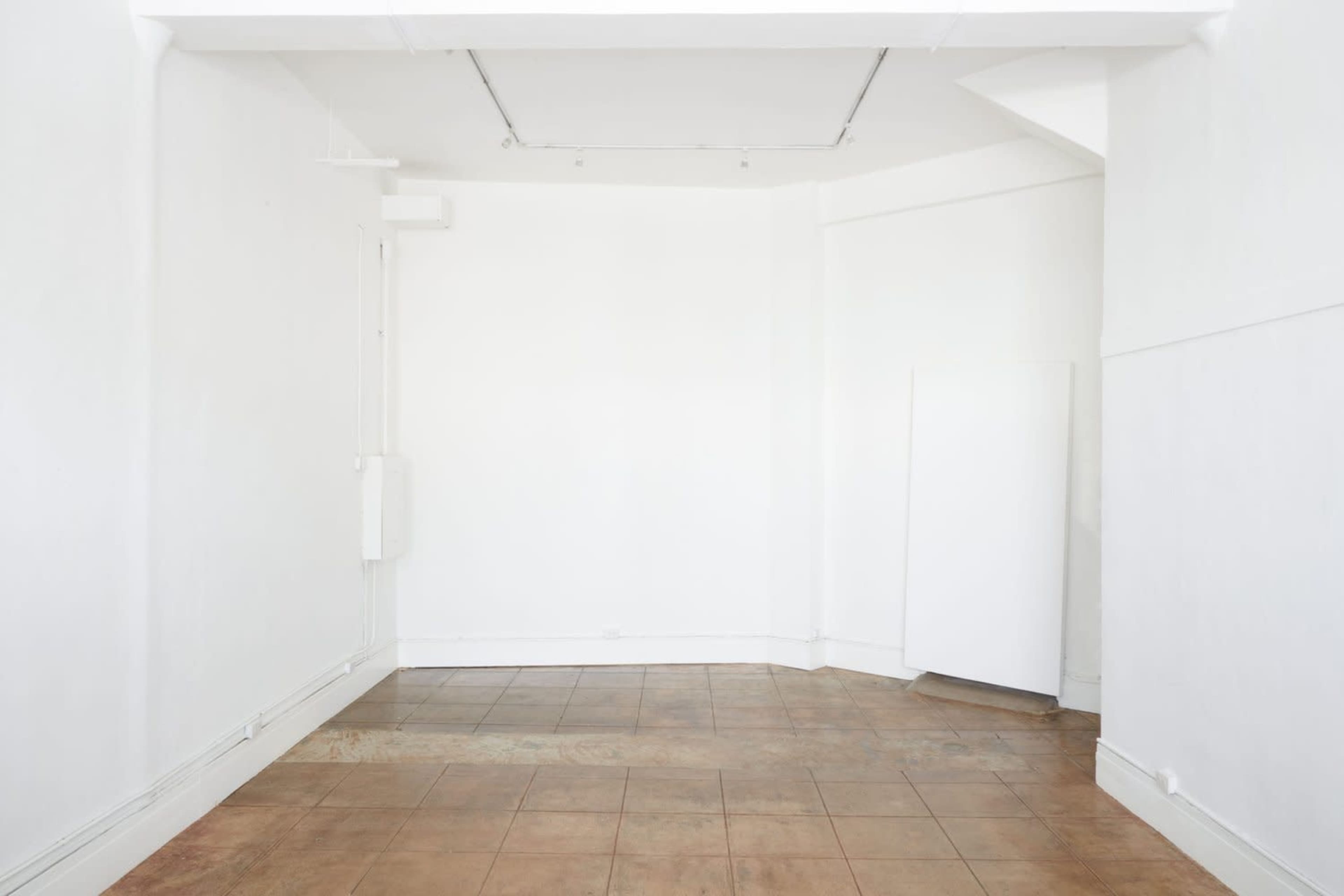 A spacious, empty room with white walls, a tiled floor, and an upright white object in the corner.