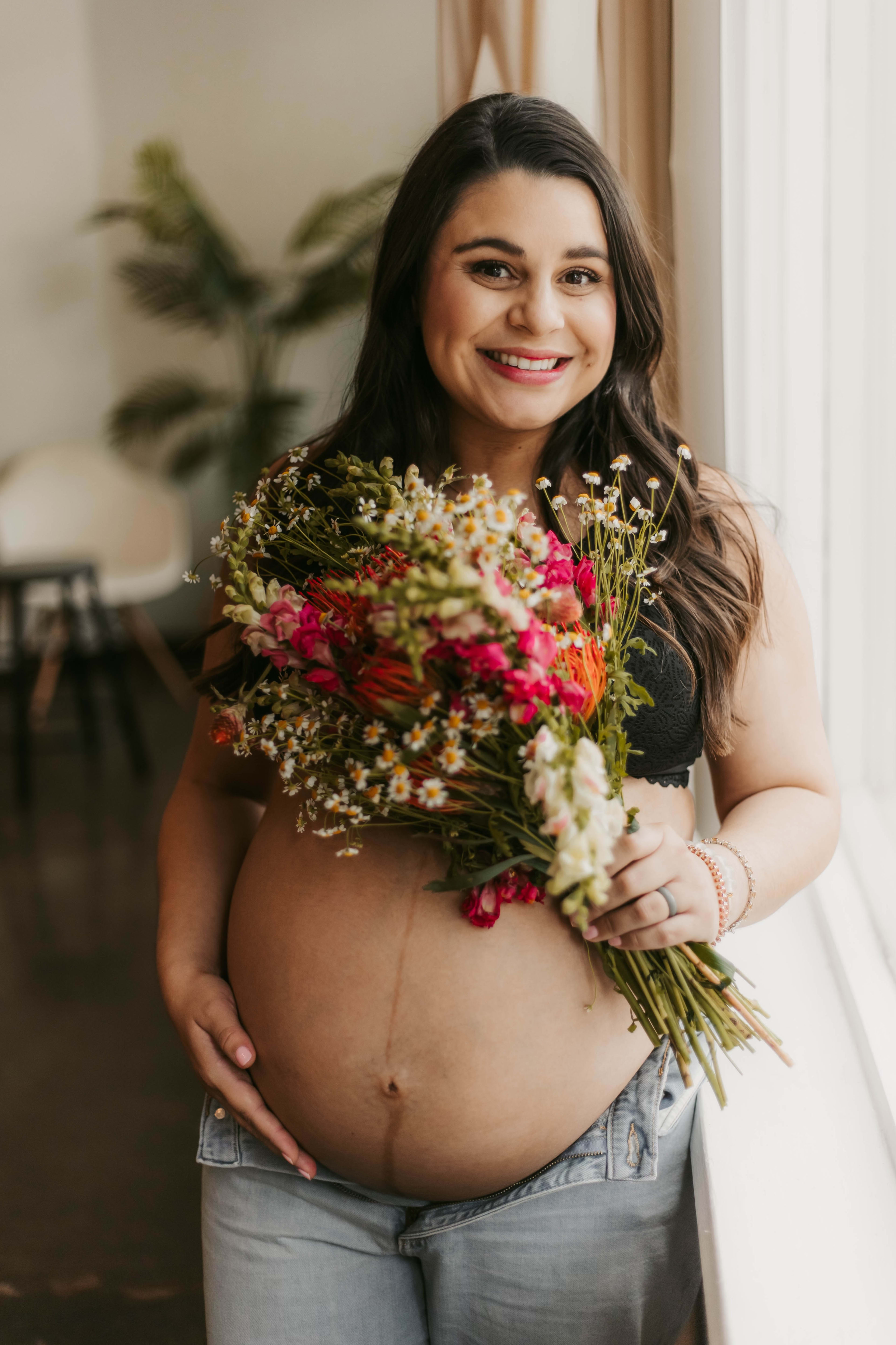 A pregnant woman in a photoshoot holding a bouquet of flowers.