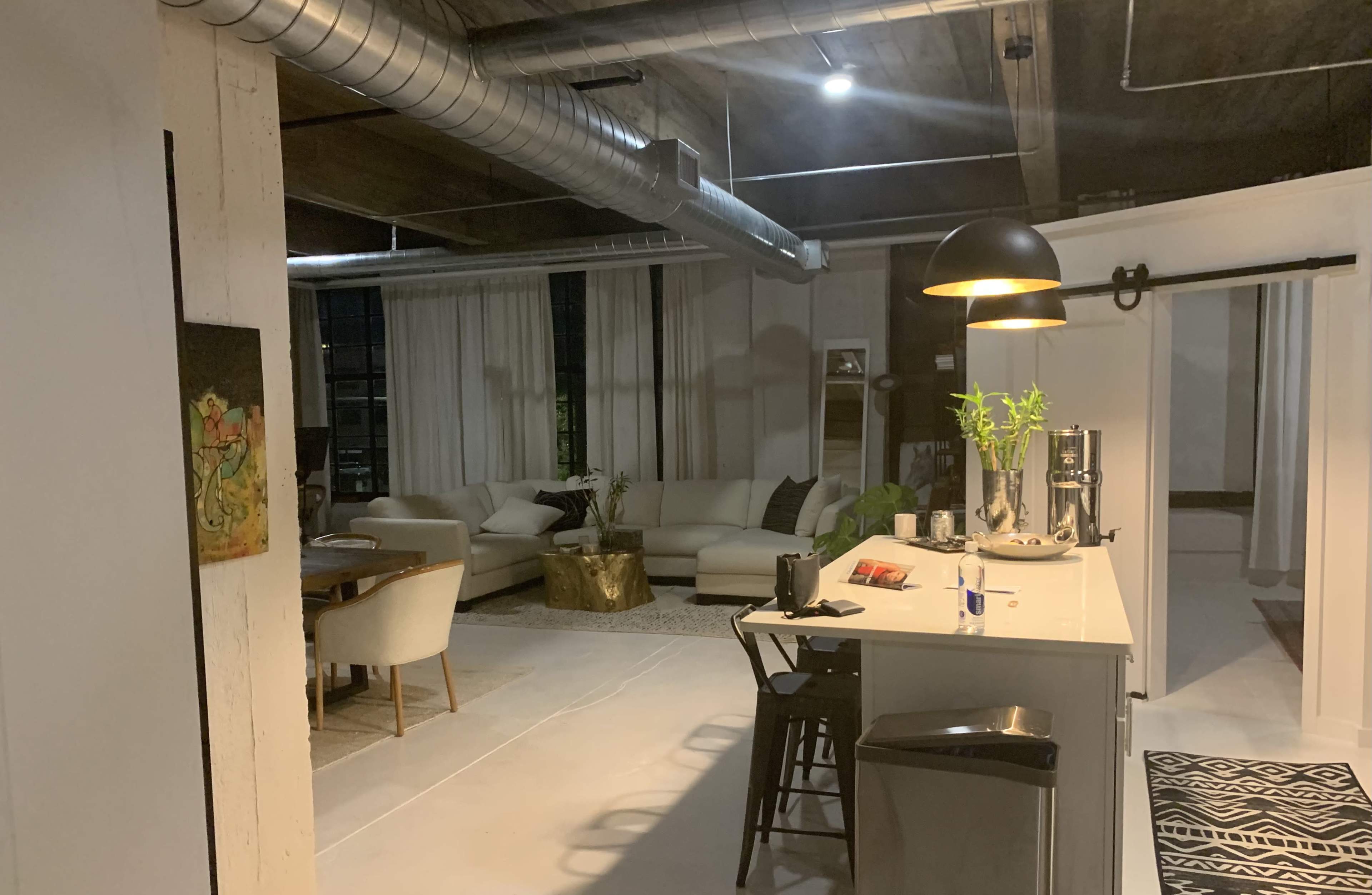 The image shows a modern, open-concept apartment with a kitchen area and a living room featuring a sofa and dining table.