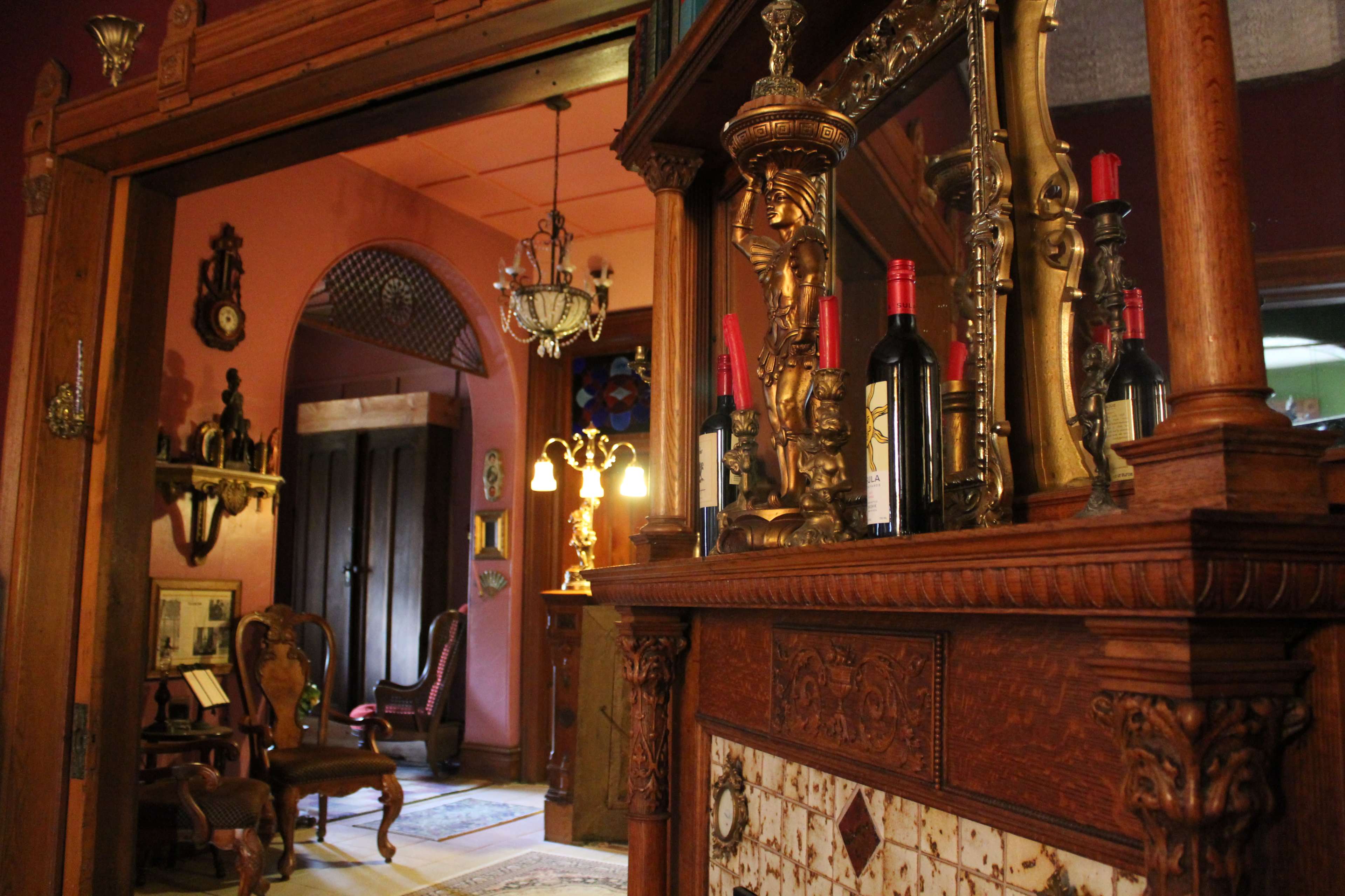 The scene shows a vintage interior with ornate wooden furnishings, a decorative fireplace, and bottles of wine displayed on a shelf, leading to an arched doorway.