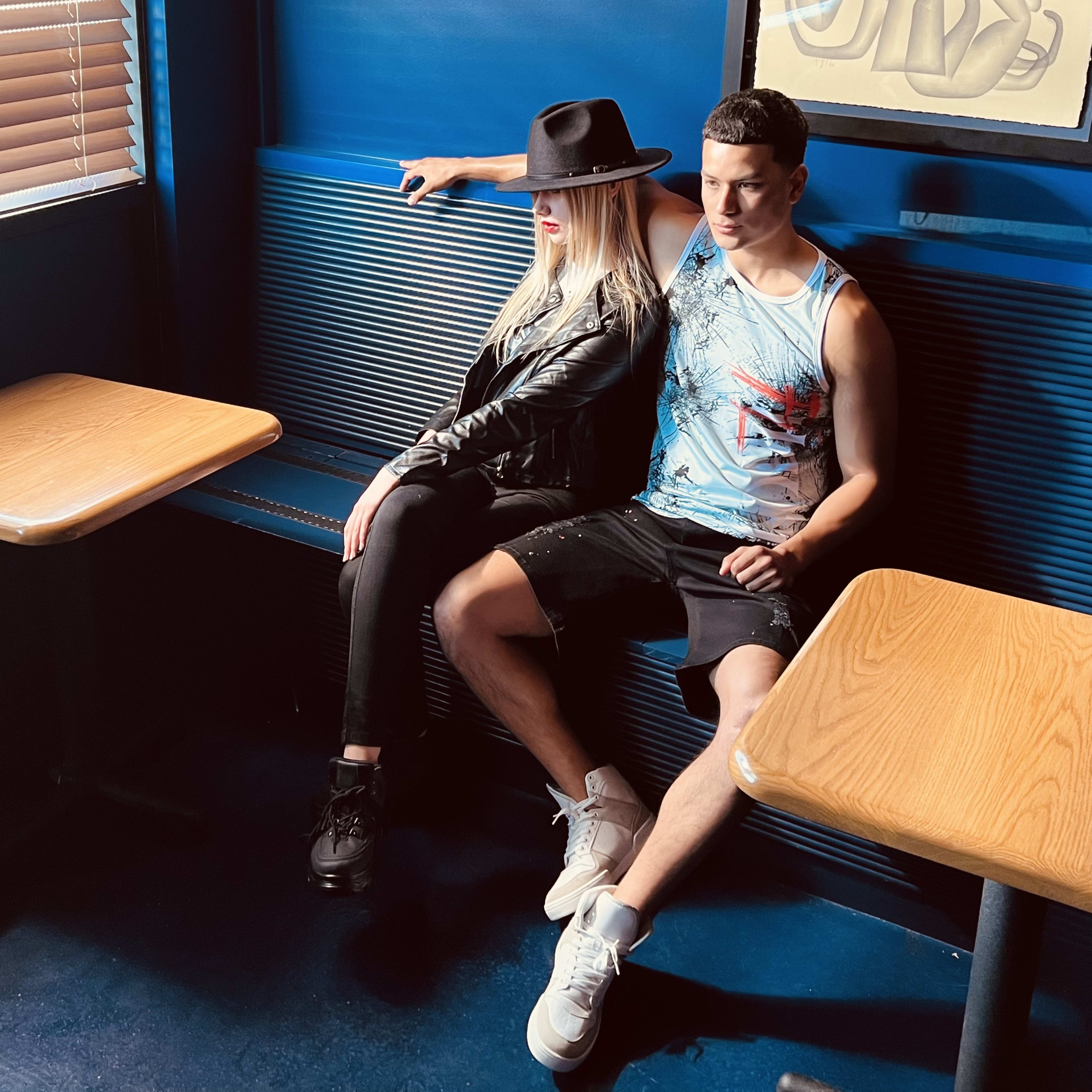 A fashion photoshoot with a man and a woman sitting on a blue bench in a restaurant.
