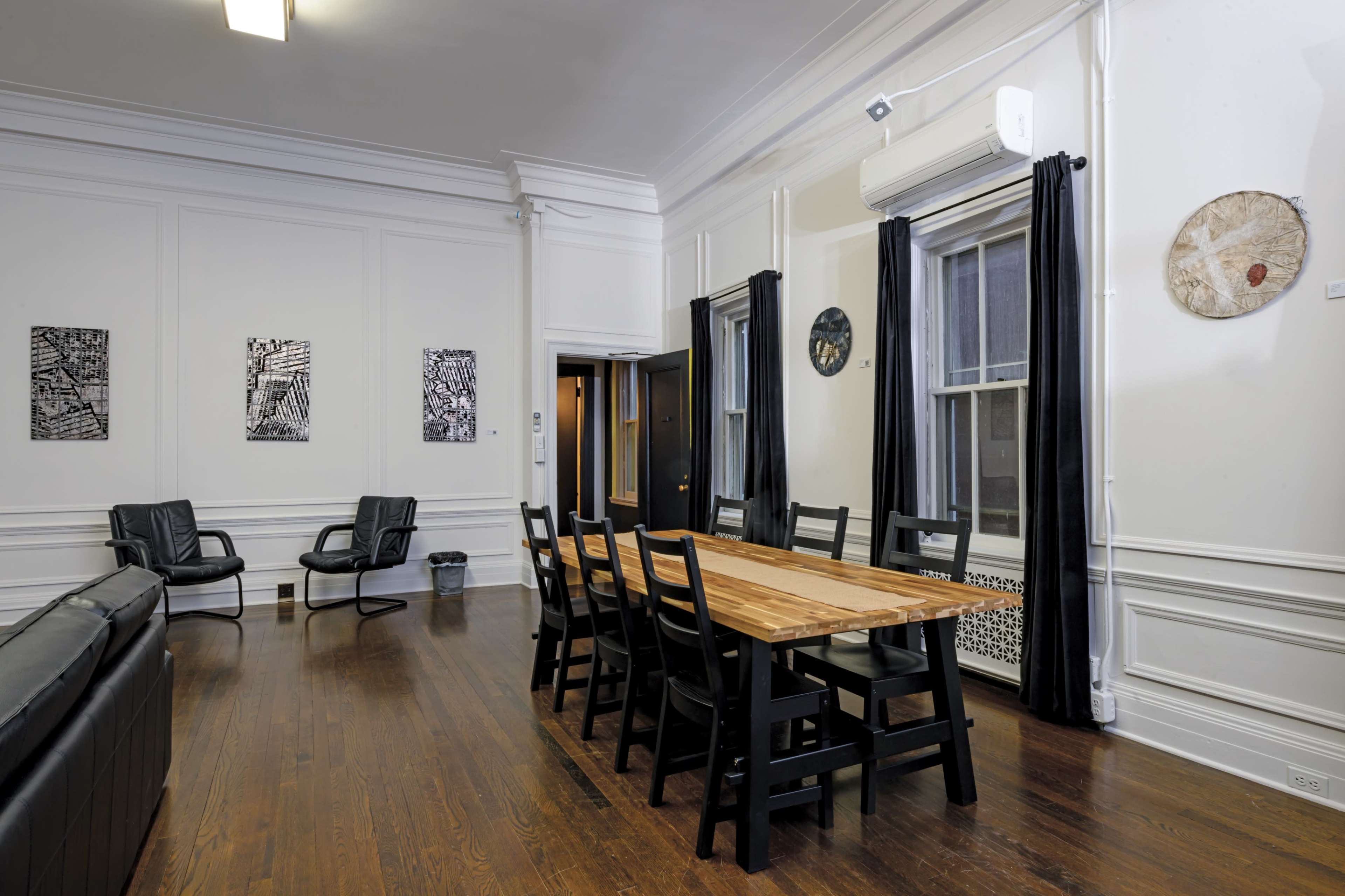 The image shows a spacious room with a wooden dining table surrounded by black chairs, two armchairs in the corner, and framed artwork on the walls.