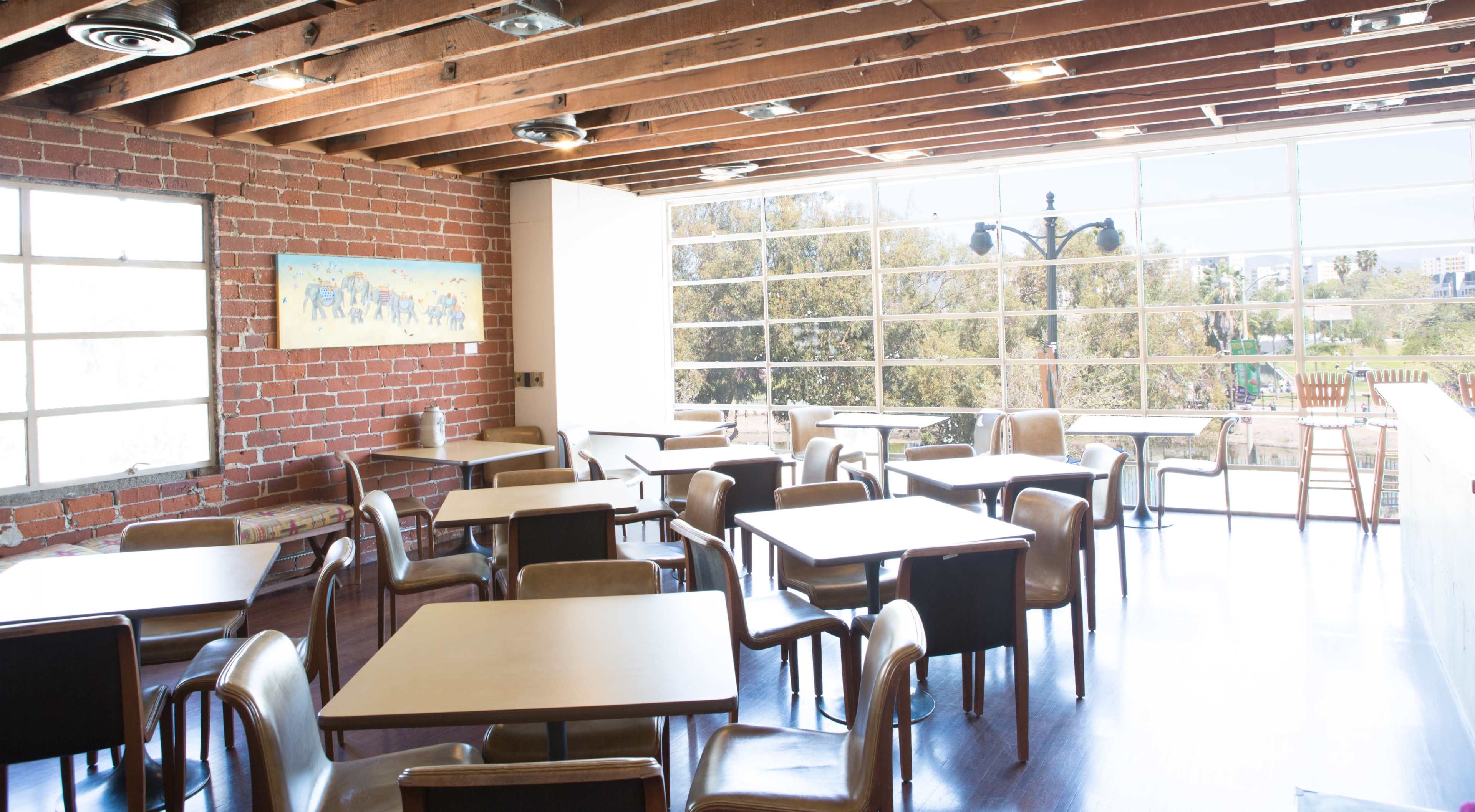 A spacious dining area with wooden beams, brick walls, and several tables and chairs arranged for seating.