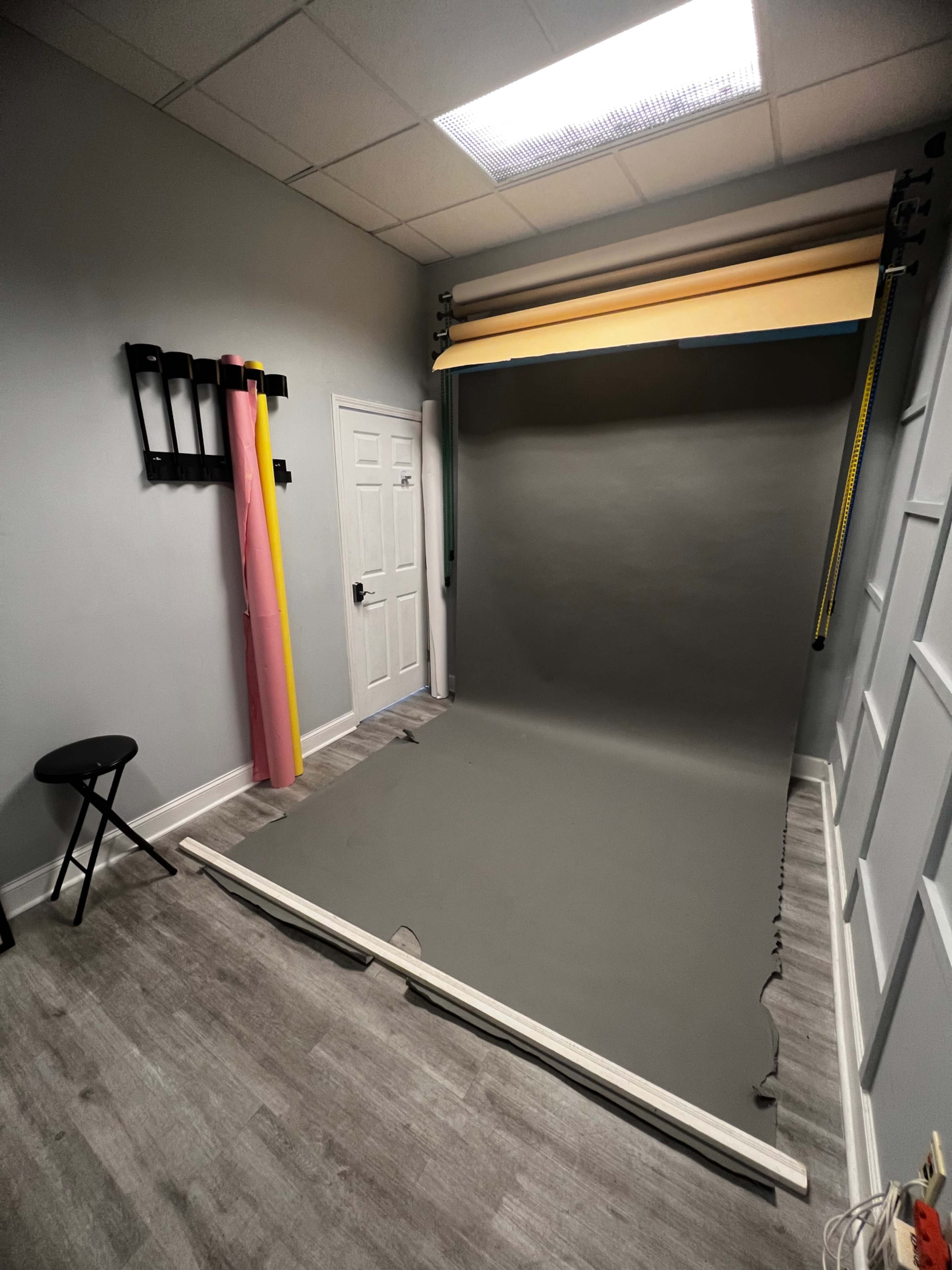 A photography studio with a gray backdrop, a stool, and colorful roll-up backdrops hanging on the wall.