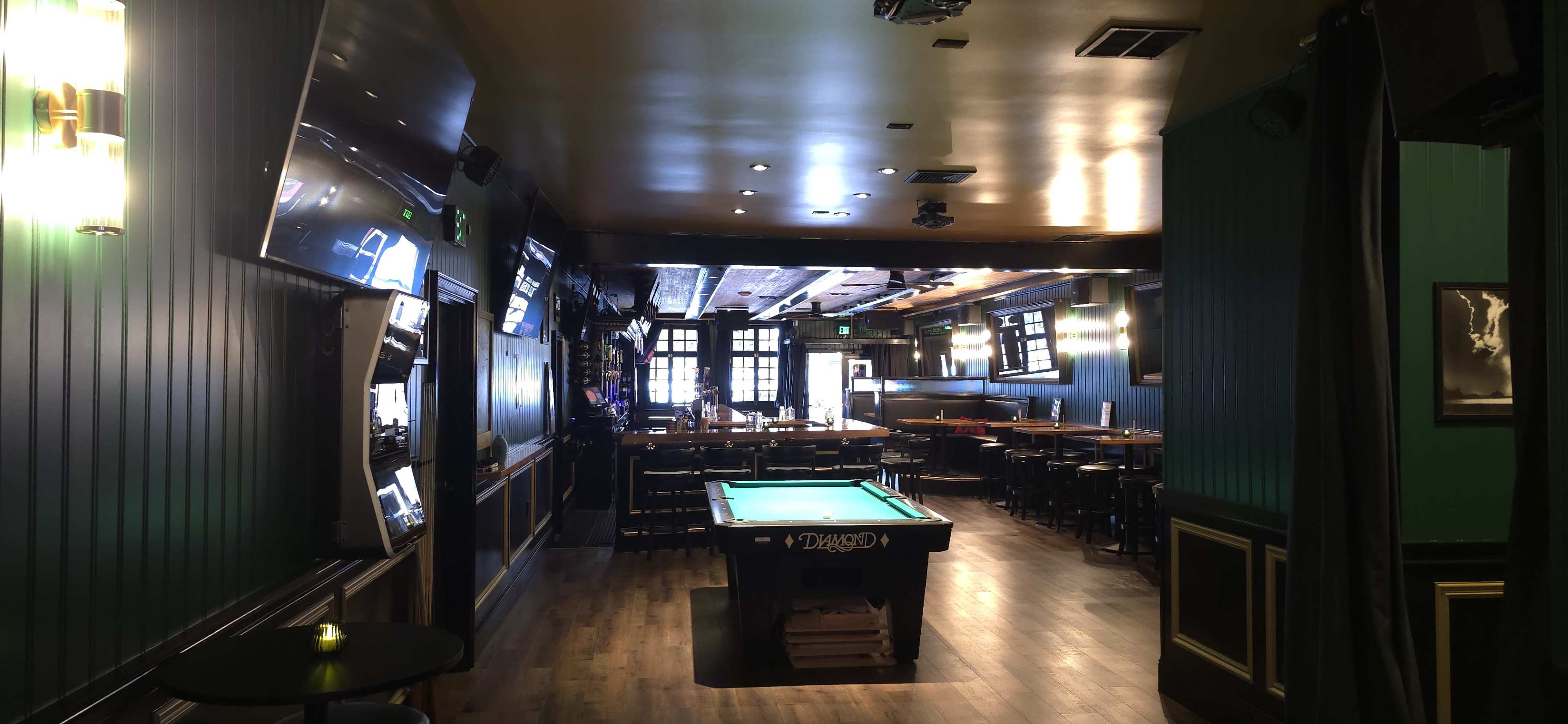 The image shows the interior of a bar or lounge featuring a pool table, seating areas, and multiple screens mounted on the walls.