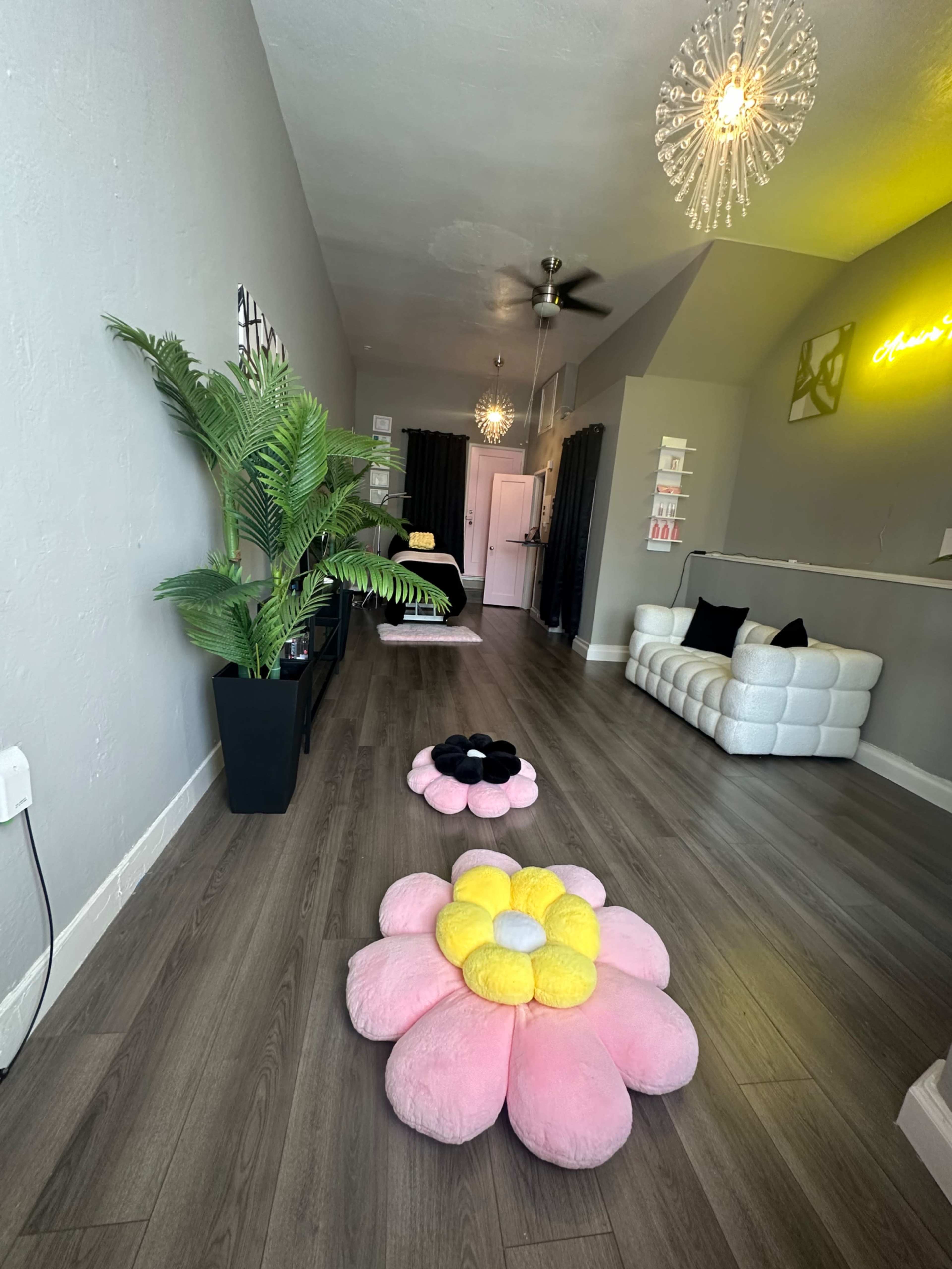 The image shows a modern interior of a room featuring decorative flower-shaped cushions on the floor, a white couch, and a plant in a pot.