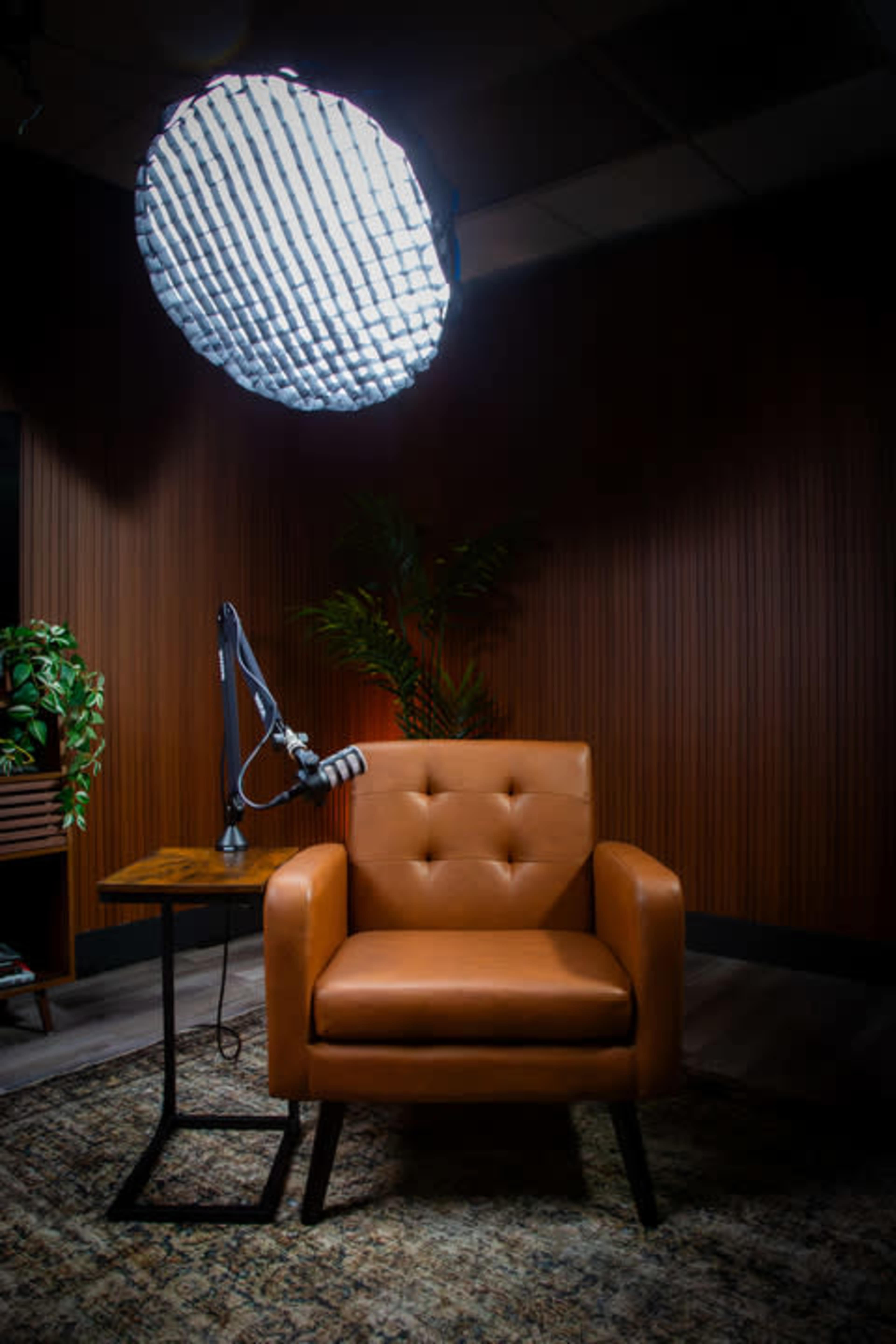 The image features a brown upholstered chair beside a small wooden table and a large overhead light source against a textured wooden wall.
