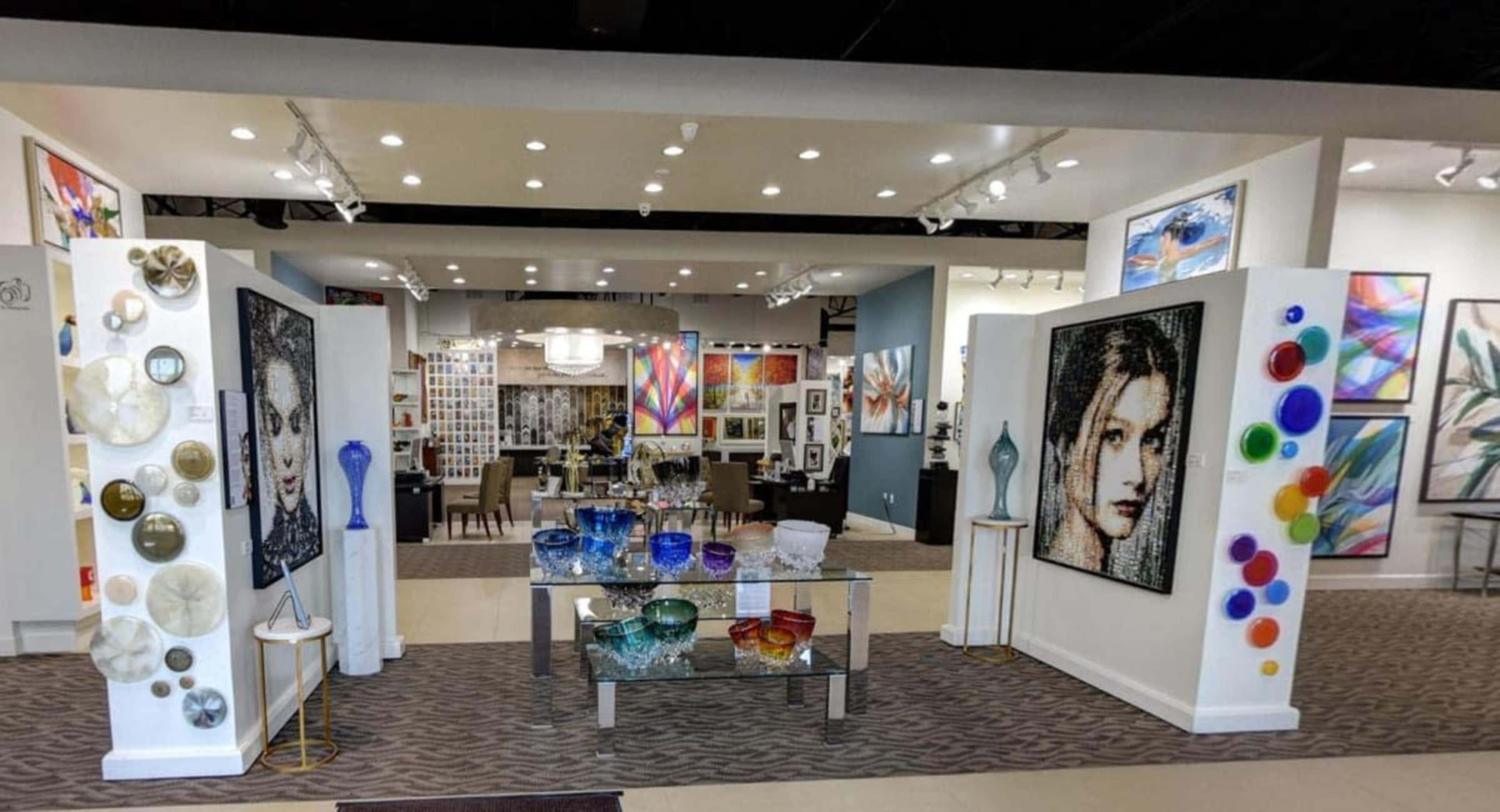 The image shows a spacious art gallery featuring colorful wall art, decorative glassware, and sculptures arranged in an inviting layout.