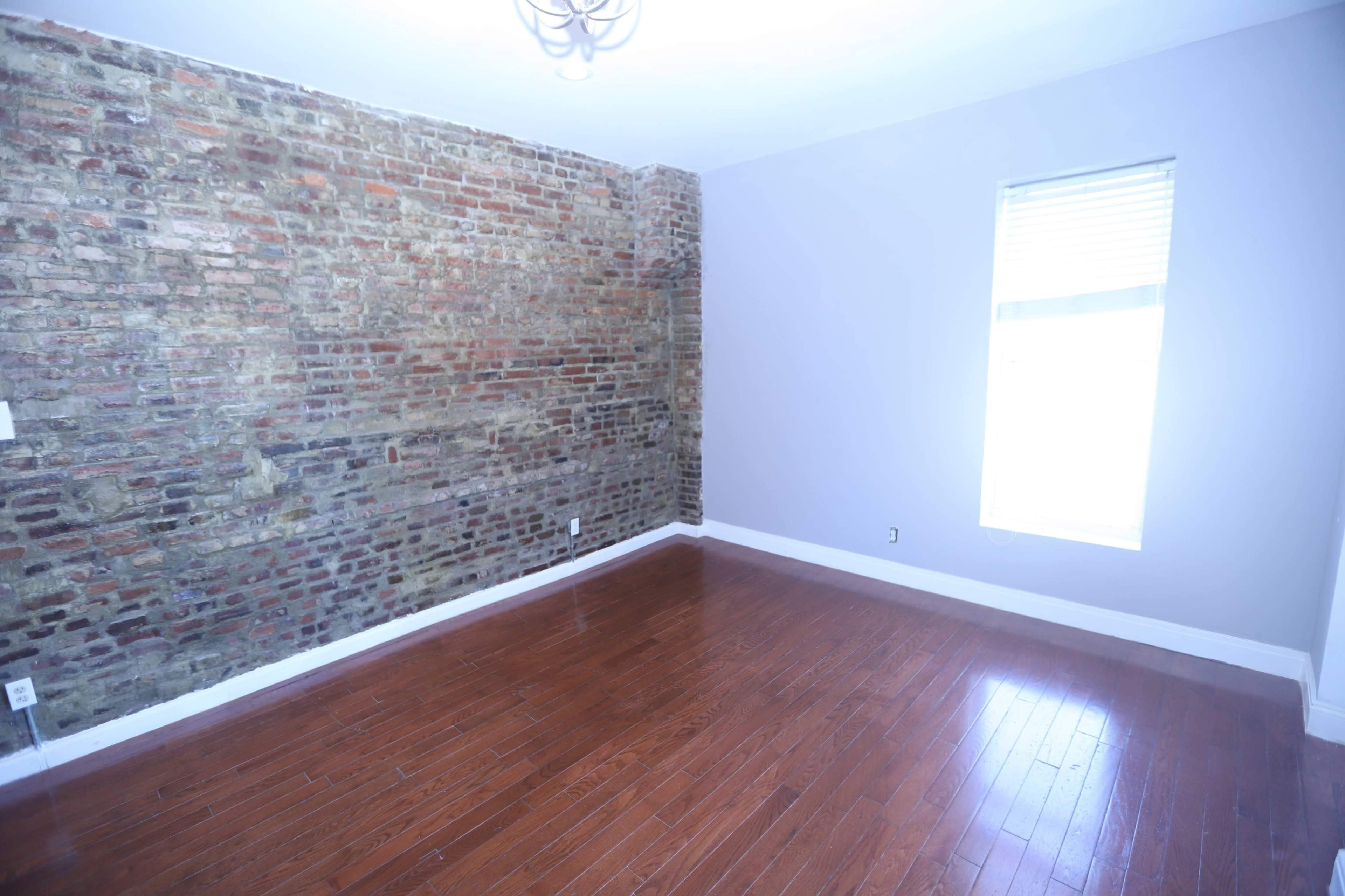 A room features a brick accent wall, hardwood flooring, and a window letting in natural light.