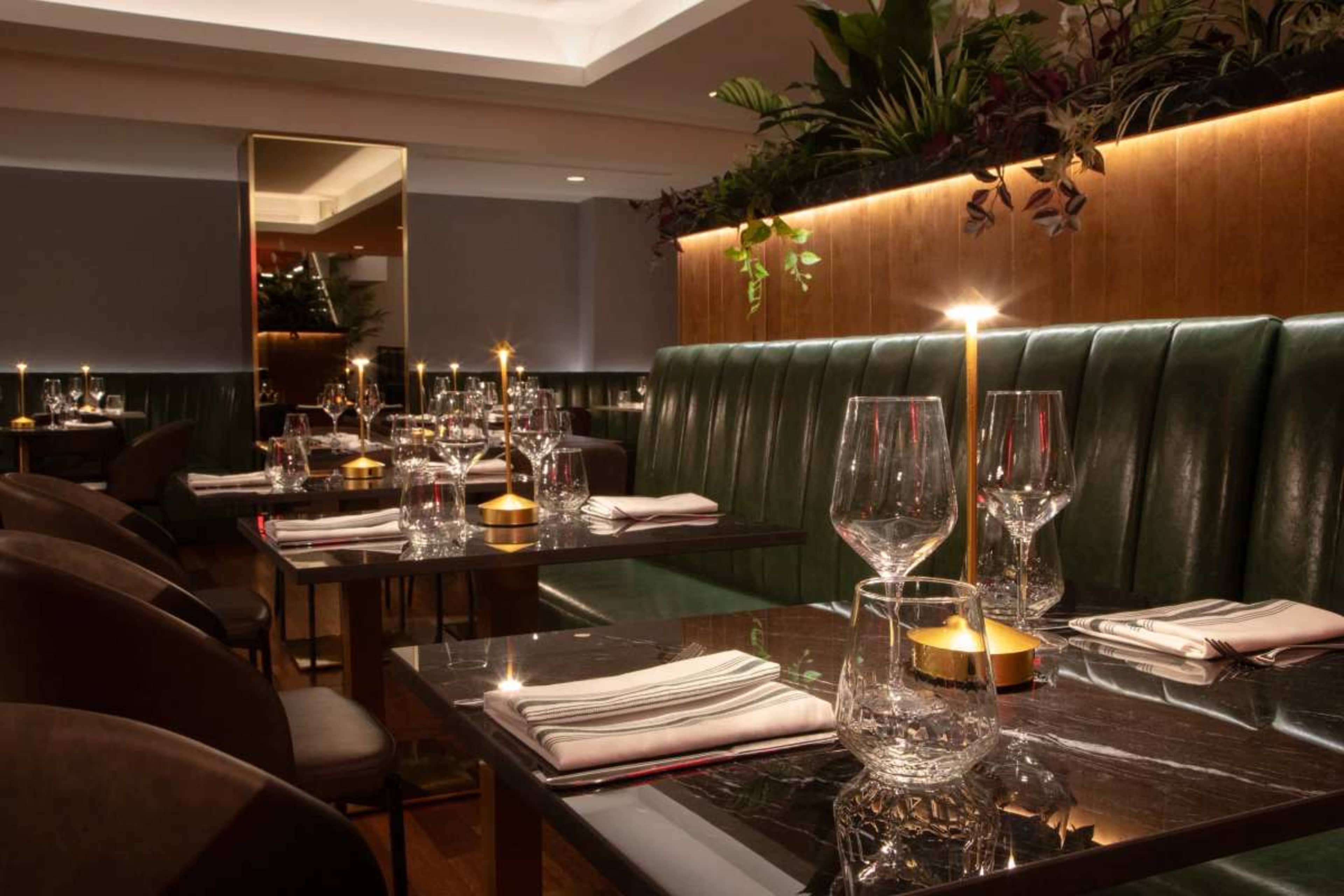 The image shows an elegantly arranged restaurant interior with green banquettes, polished tables, and soft lighting from candles.