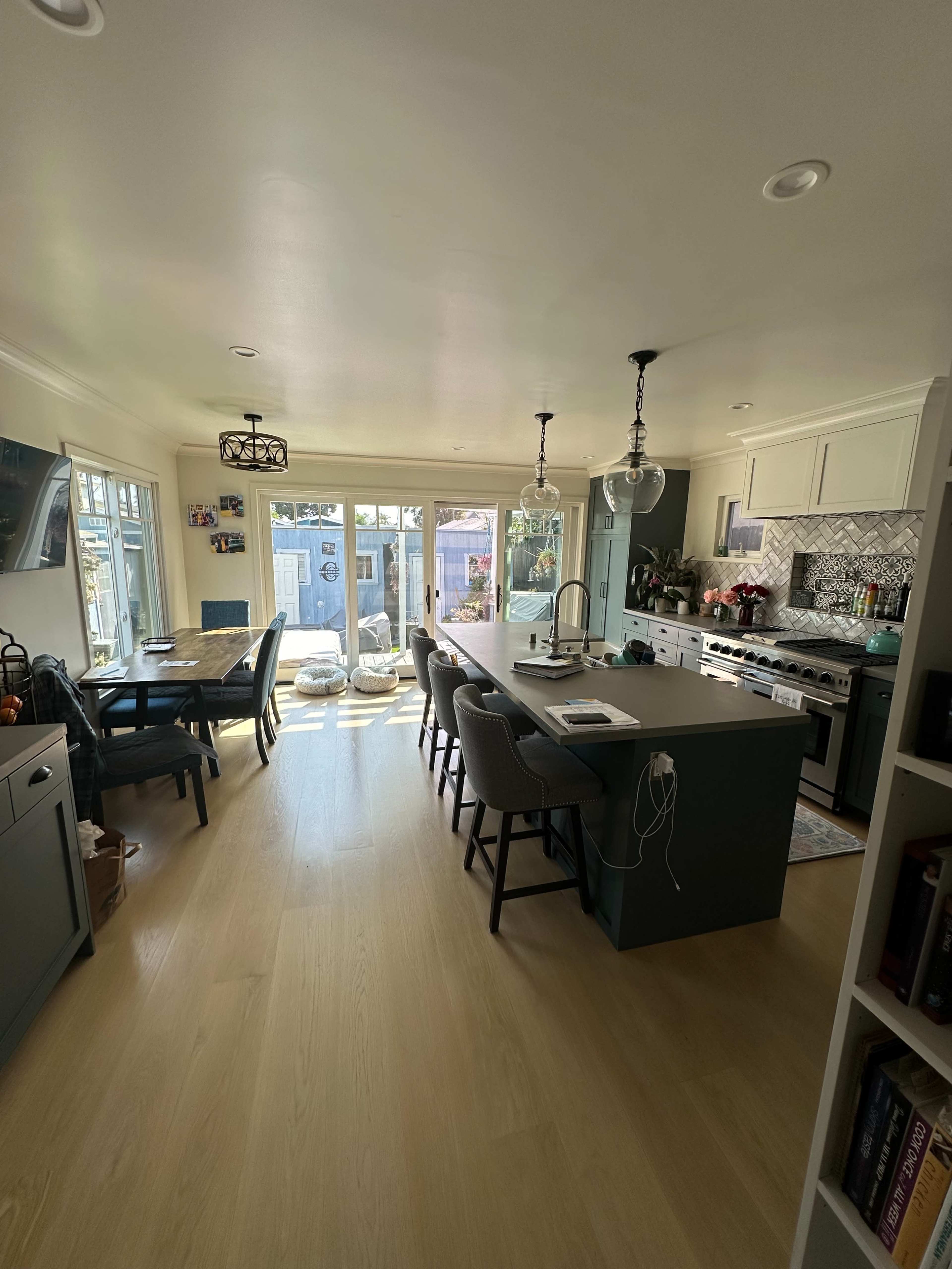 A spacious kitchen features a central island with bar seating, a dining table, large windows, and modern appliances.