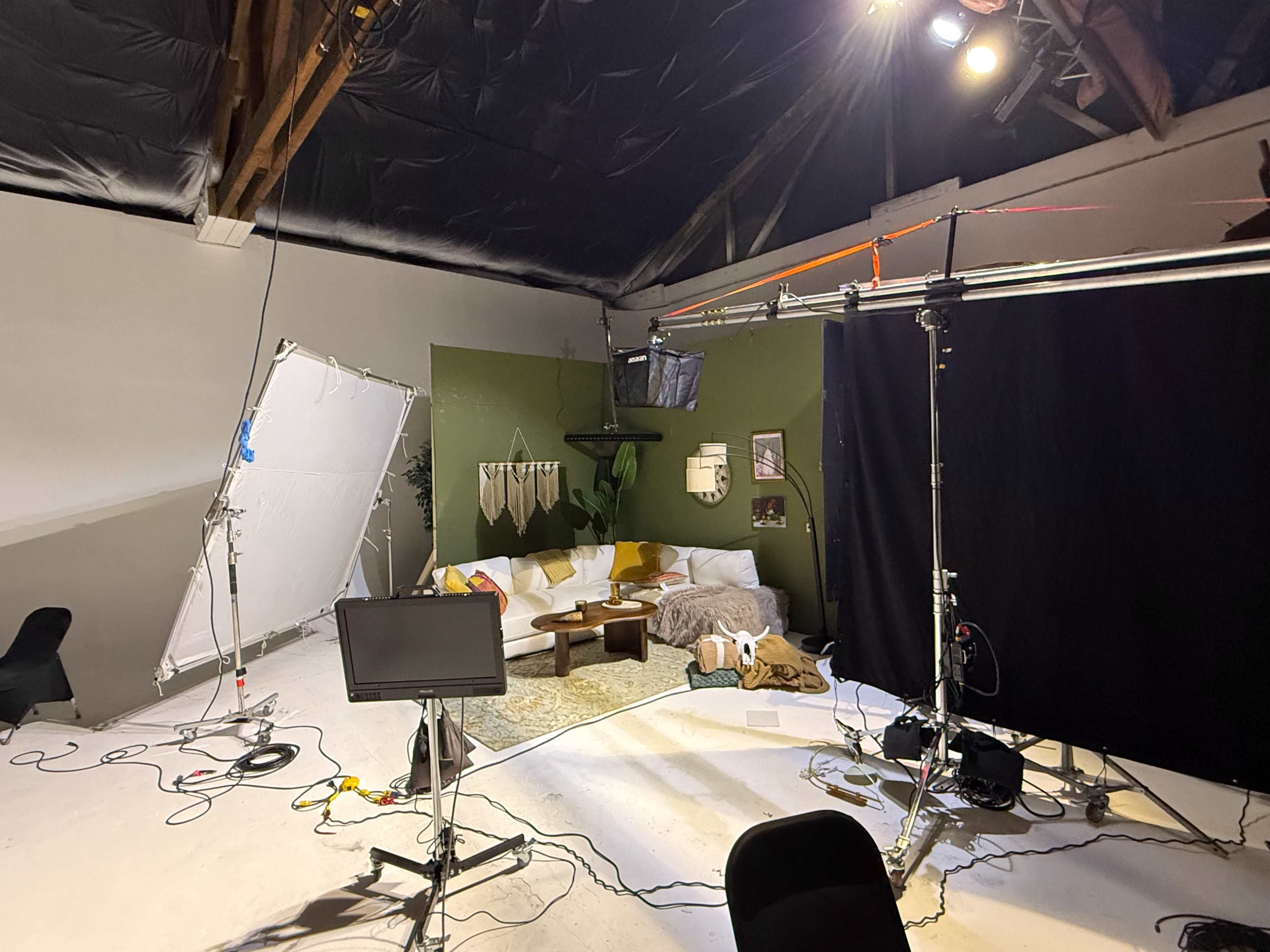 The image shows a studio setup with a green wall, a couch, lighting equipment, and a backdrop.