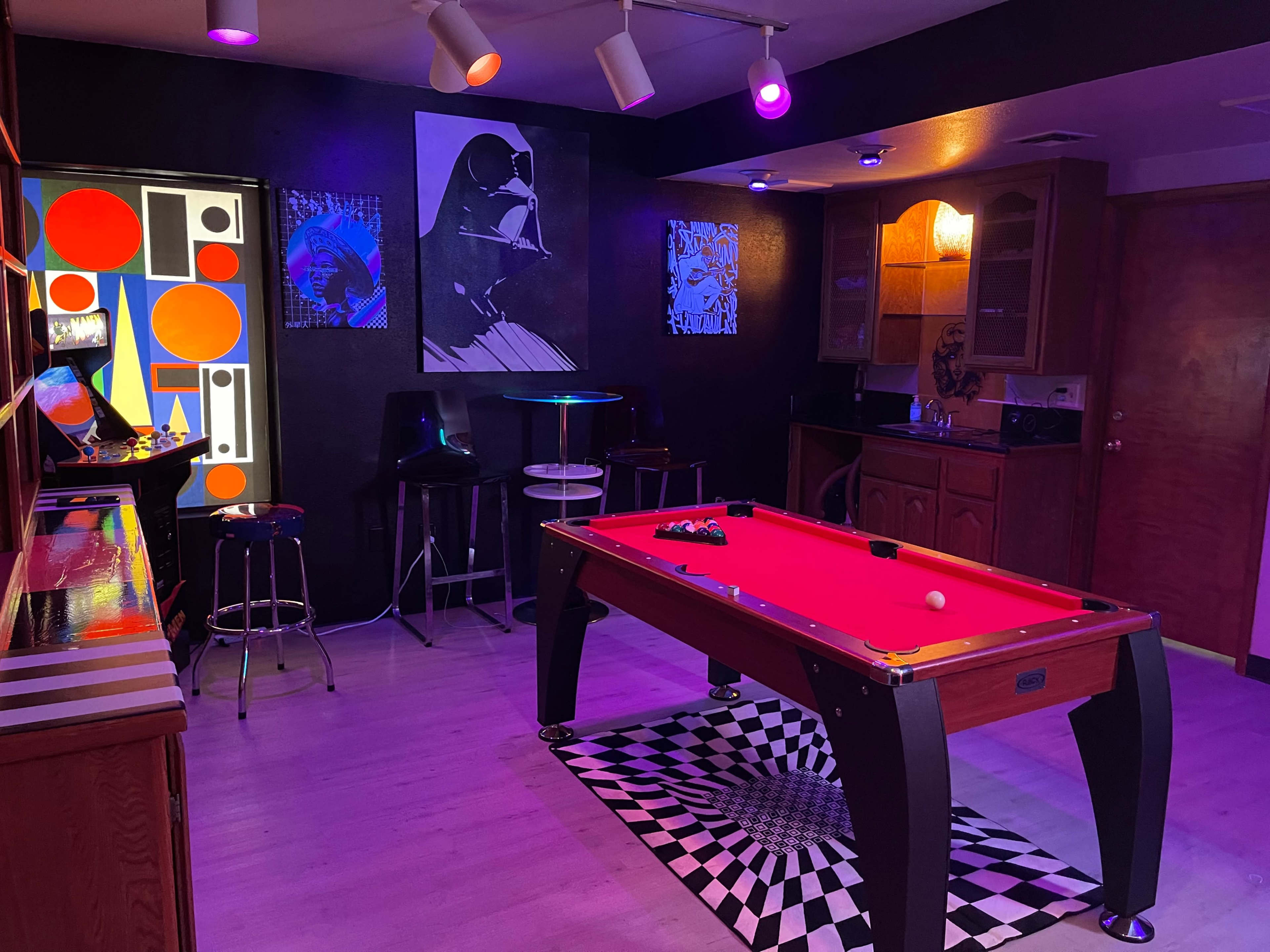 A game room featuring a red pool table, black and white checkered flooring, and colorful wall art.