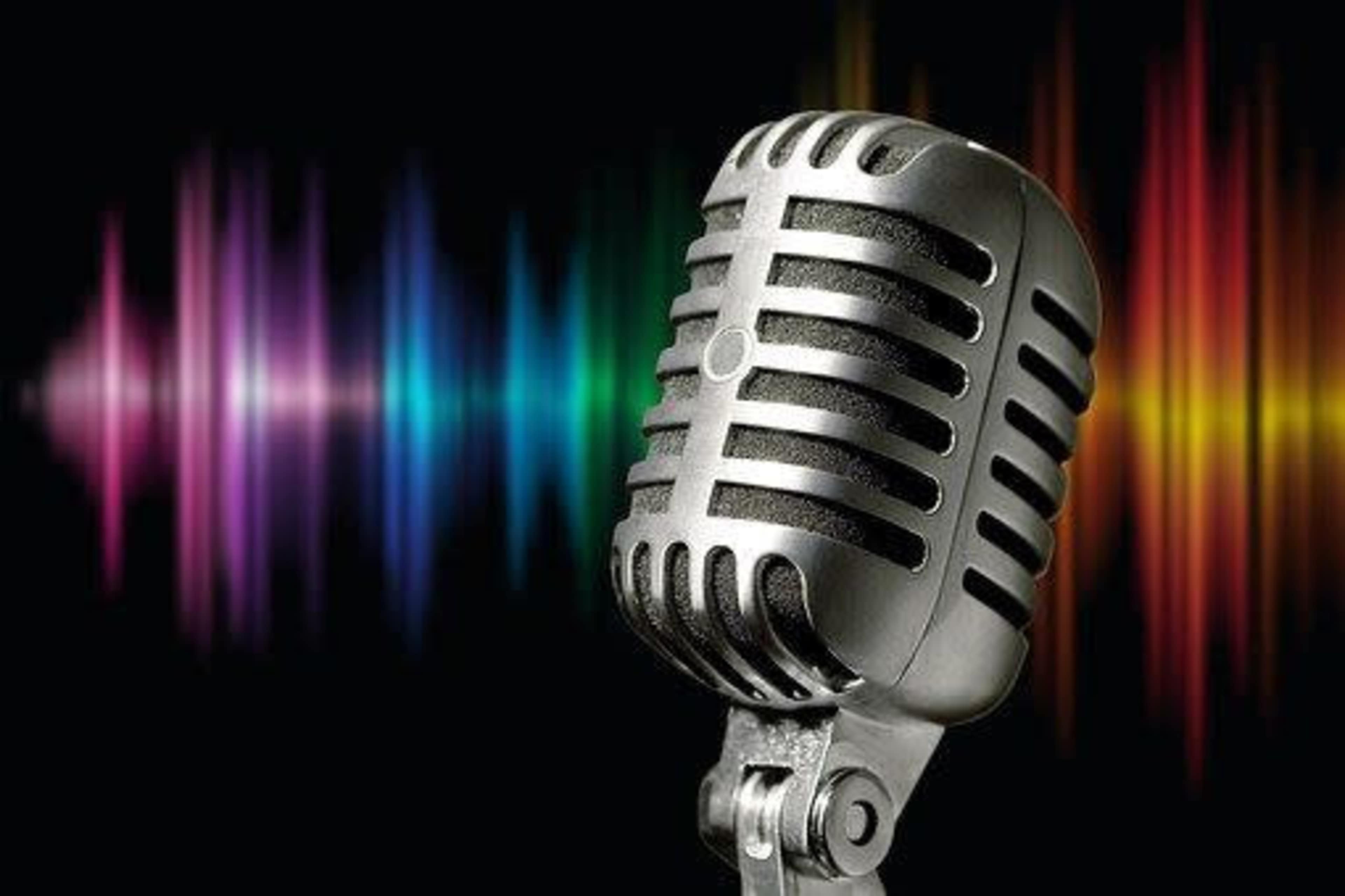 A vintage microphone is positioned in front of a colorful soundwave graphic on a black background.