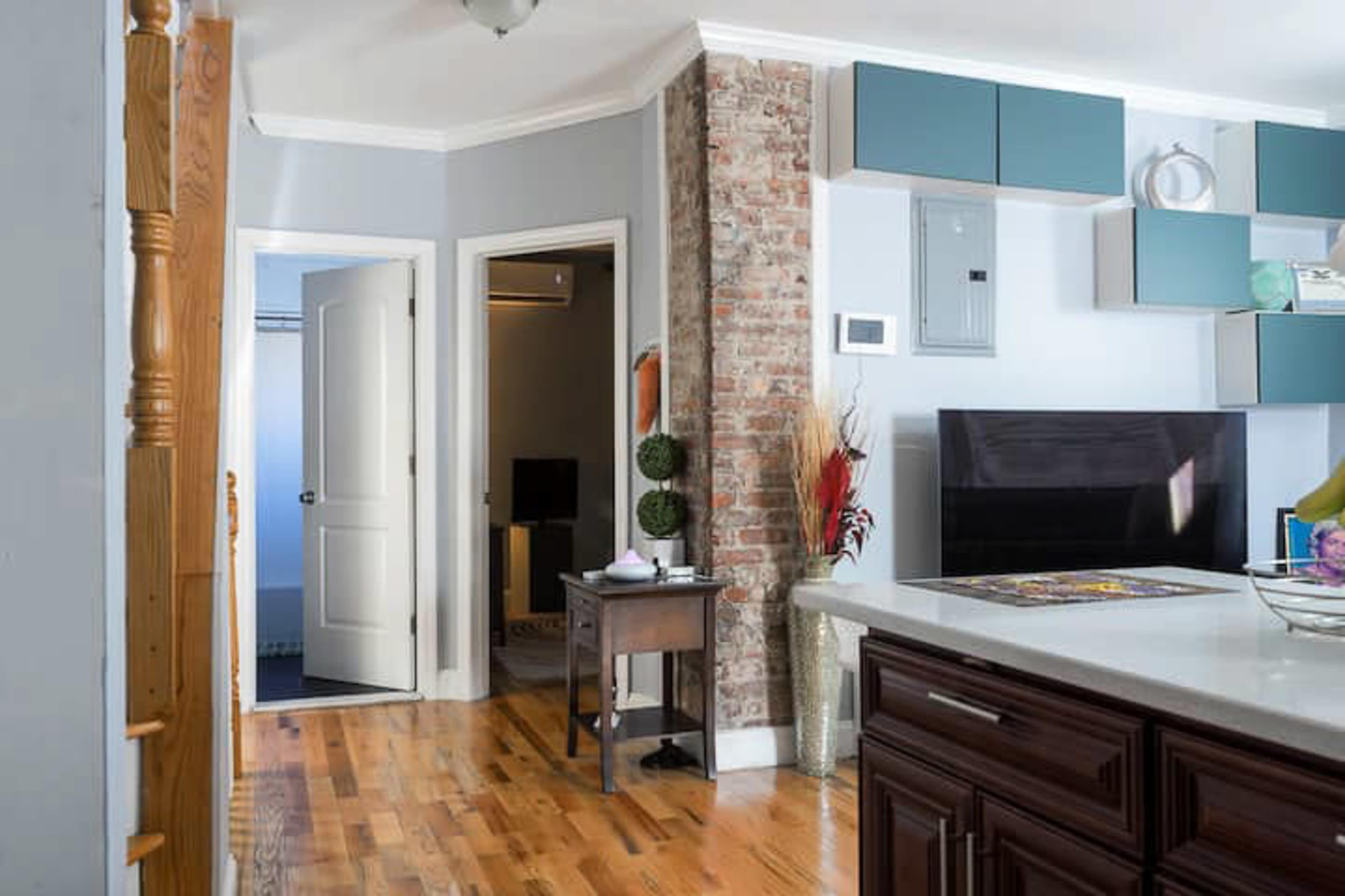 A modern kitchen area with a wooden floor, a large kitchen island, and a doorway leading to a hallway that connects to other rooms.