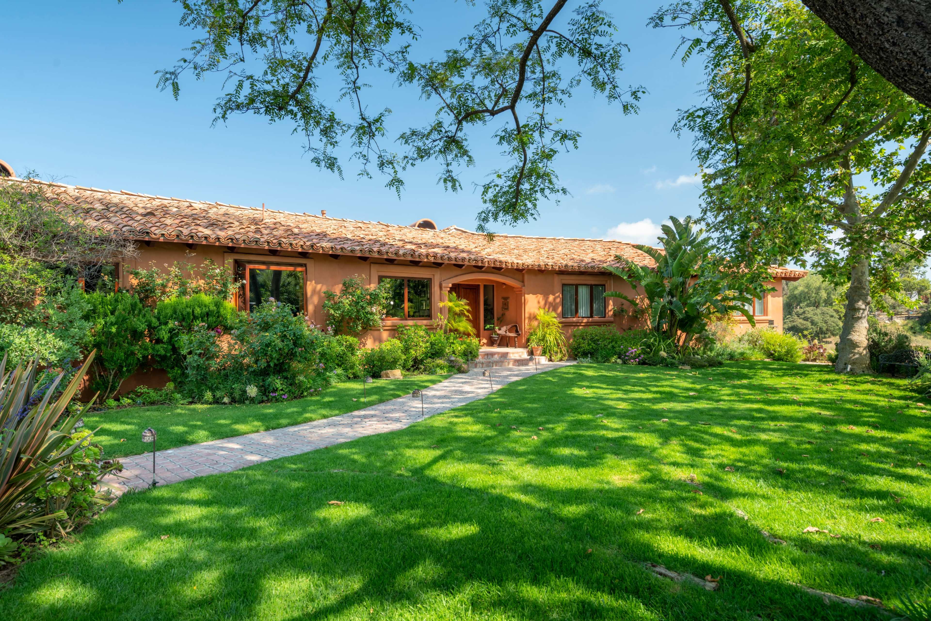 A two-story house with a tiled roof is surrounded by a lush green lawn and trees.