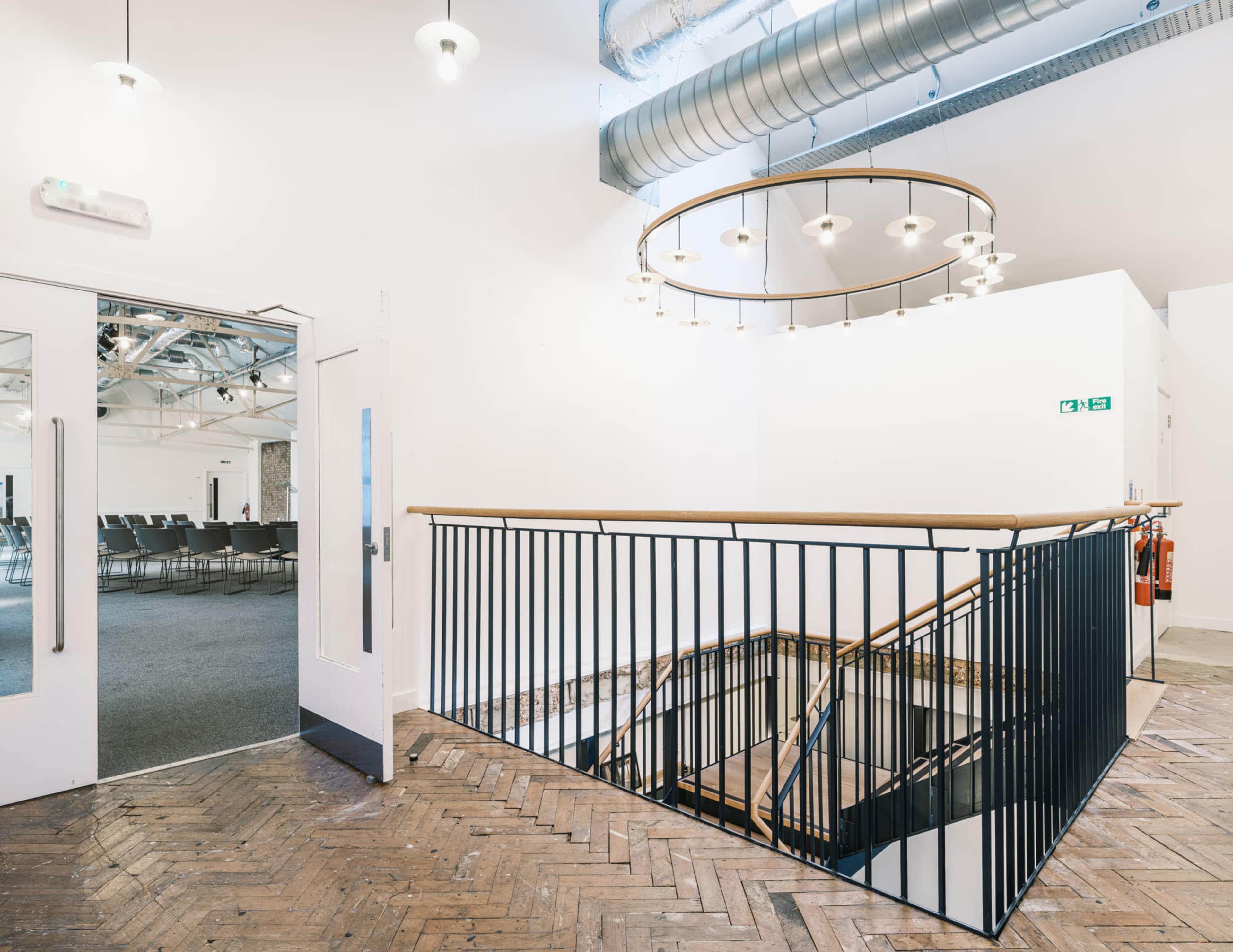 A spacious interior with a staircase, lit by circular pendant lights and featuring a dark railing, leading to an upper level.