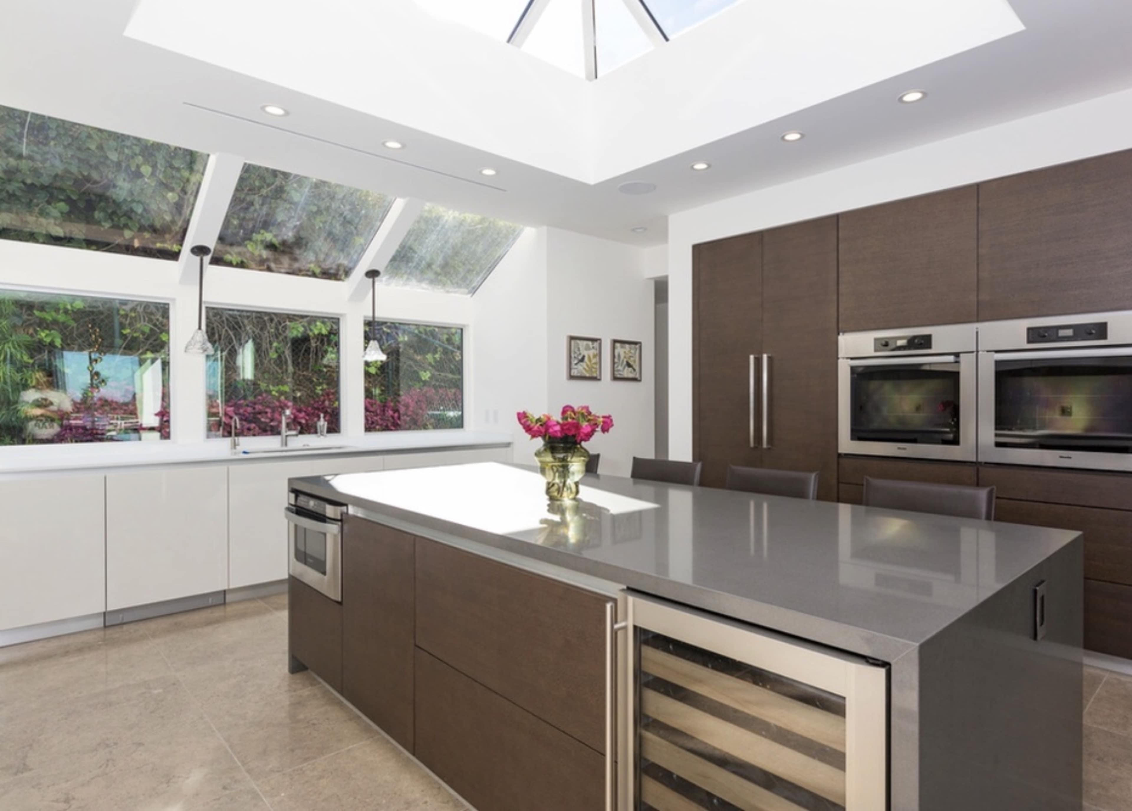 The modern kitchen features a central island with a dark countertop, double ovens, and large windows that allow natural light to fill the space.