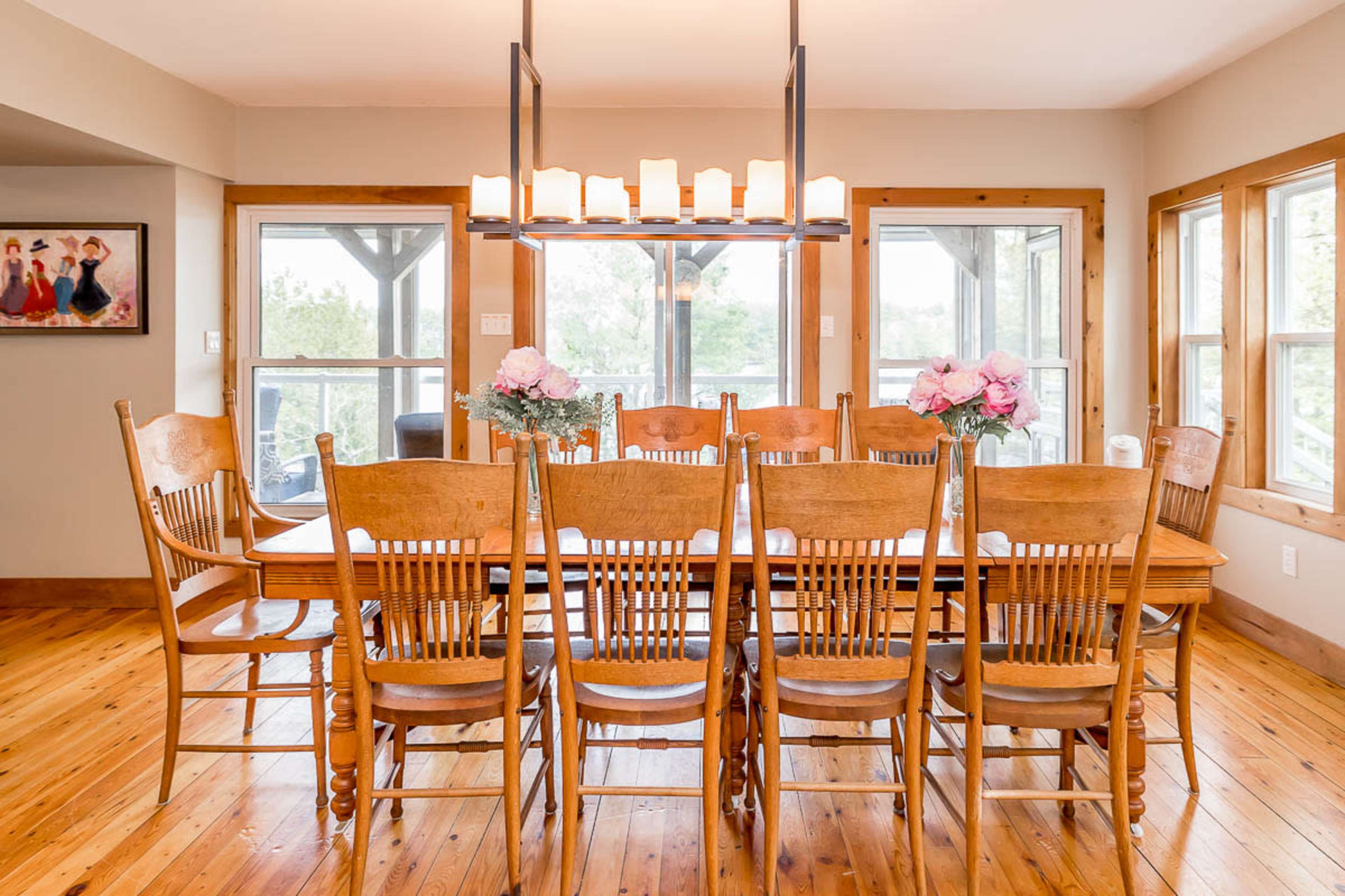 A spacious dining room features a long wooden table surrounded by several high-backed chairs, with large windows allowing natural light to fill the space.