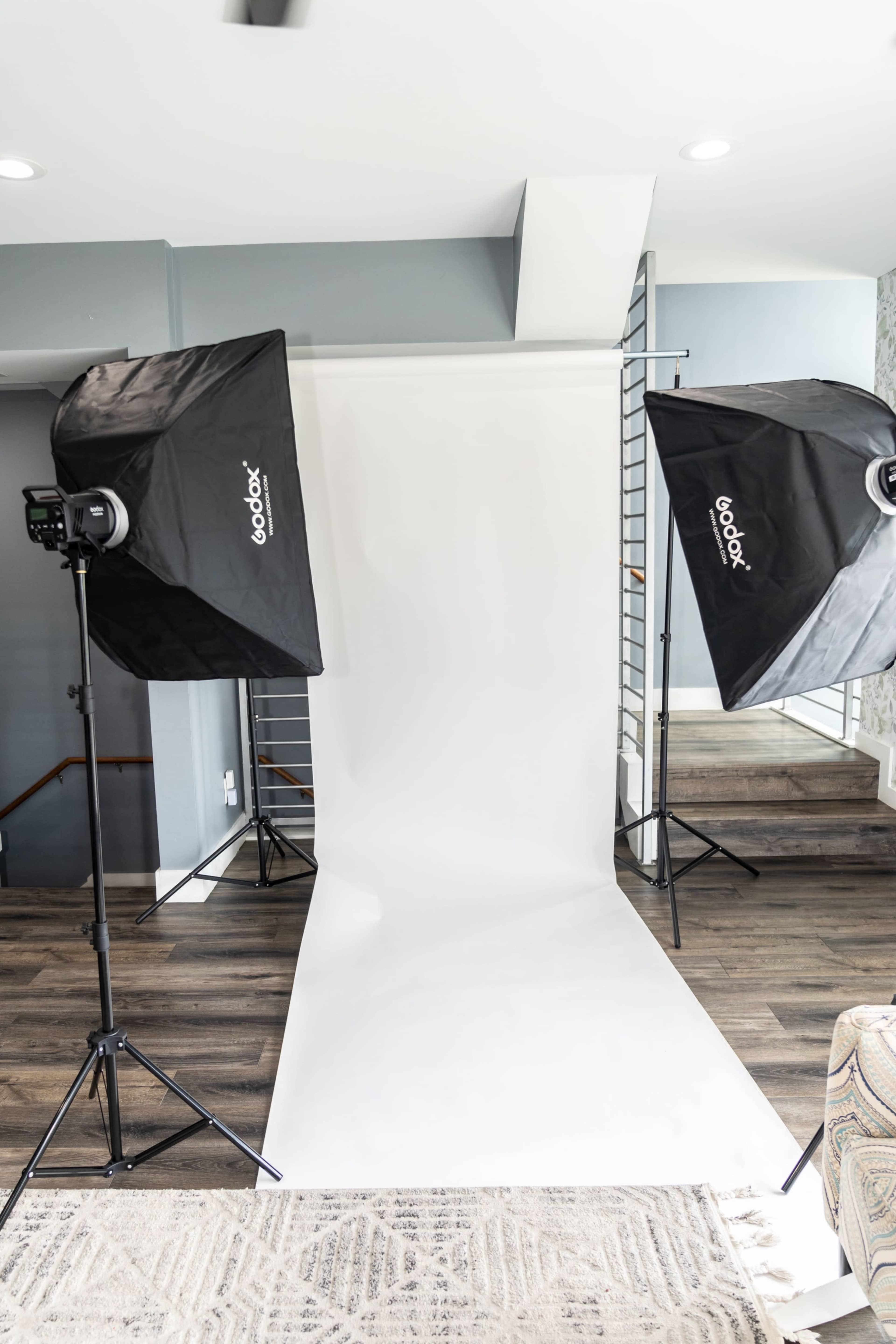 A photography studio setup with two softbox lights positioned on either side of a white backdrop and floor.