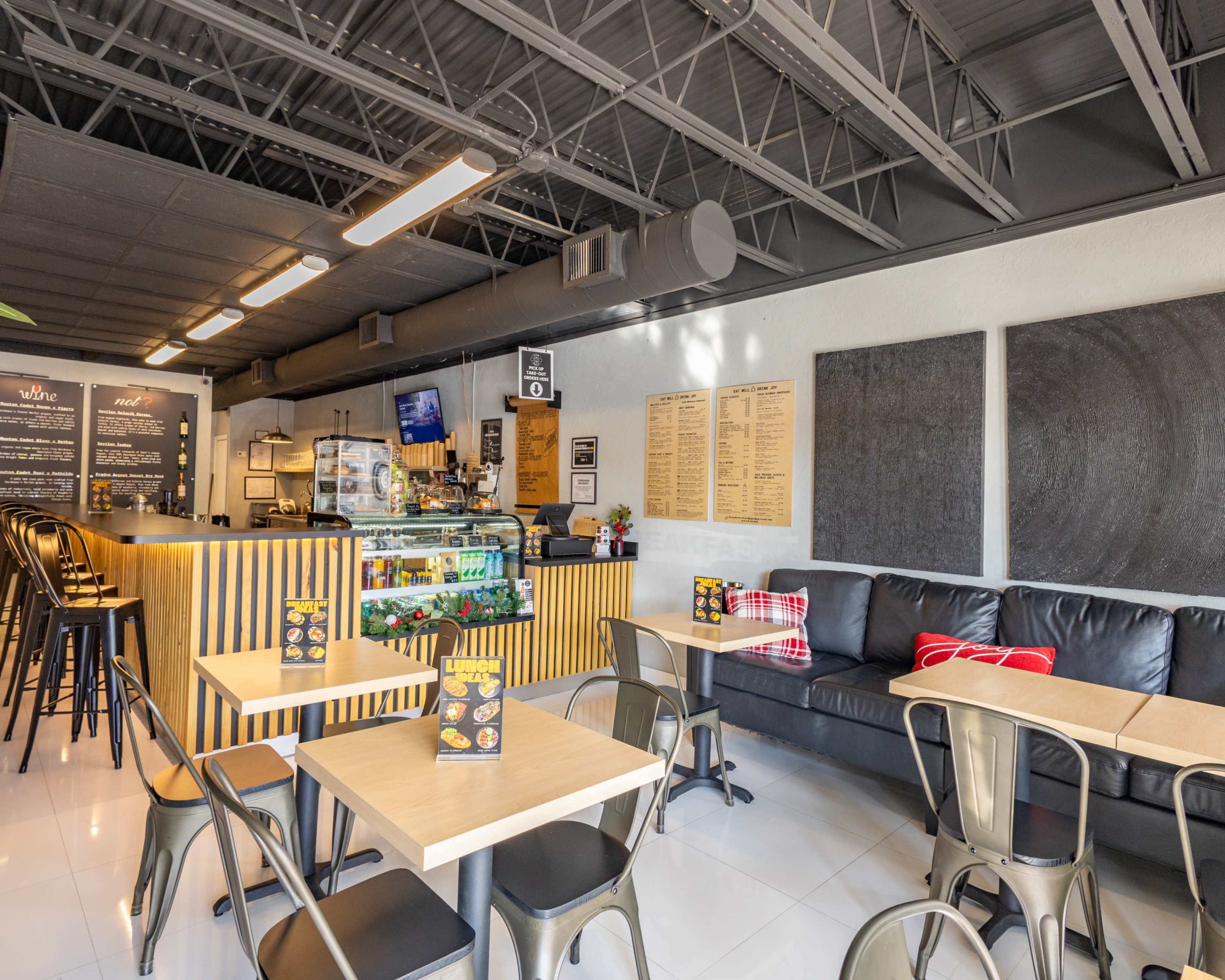 The image shows a modern café interior with wooden countertops, metal stools, and cozy seating areas.