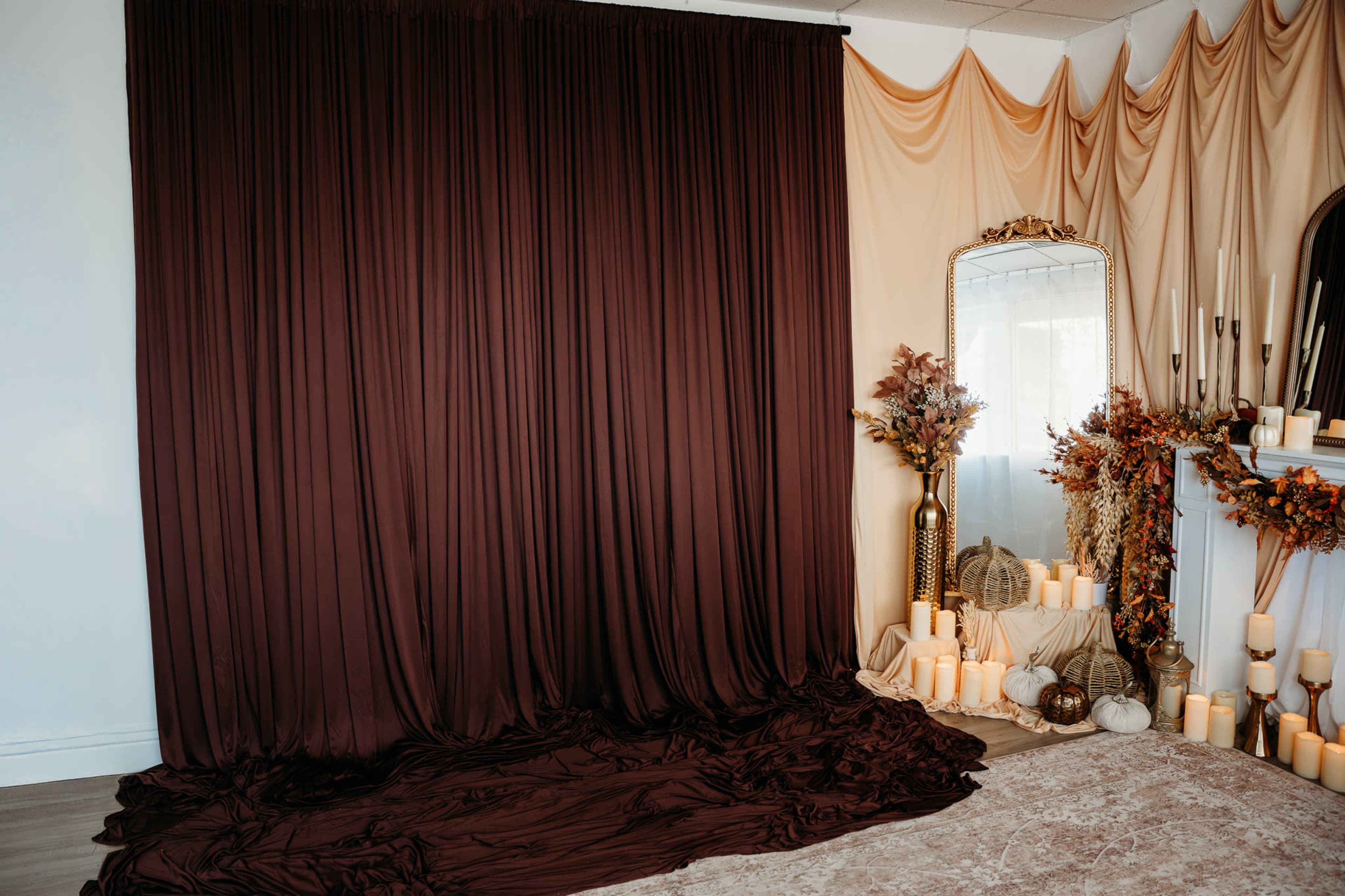 The scene features a decorated space with flowing brown fabric draped on the walls and floor, a large mirror, decorative candles, and autumnal plant arrangements.