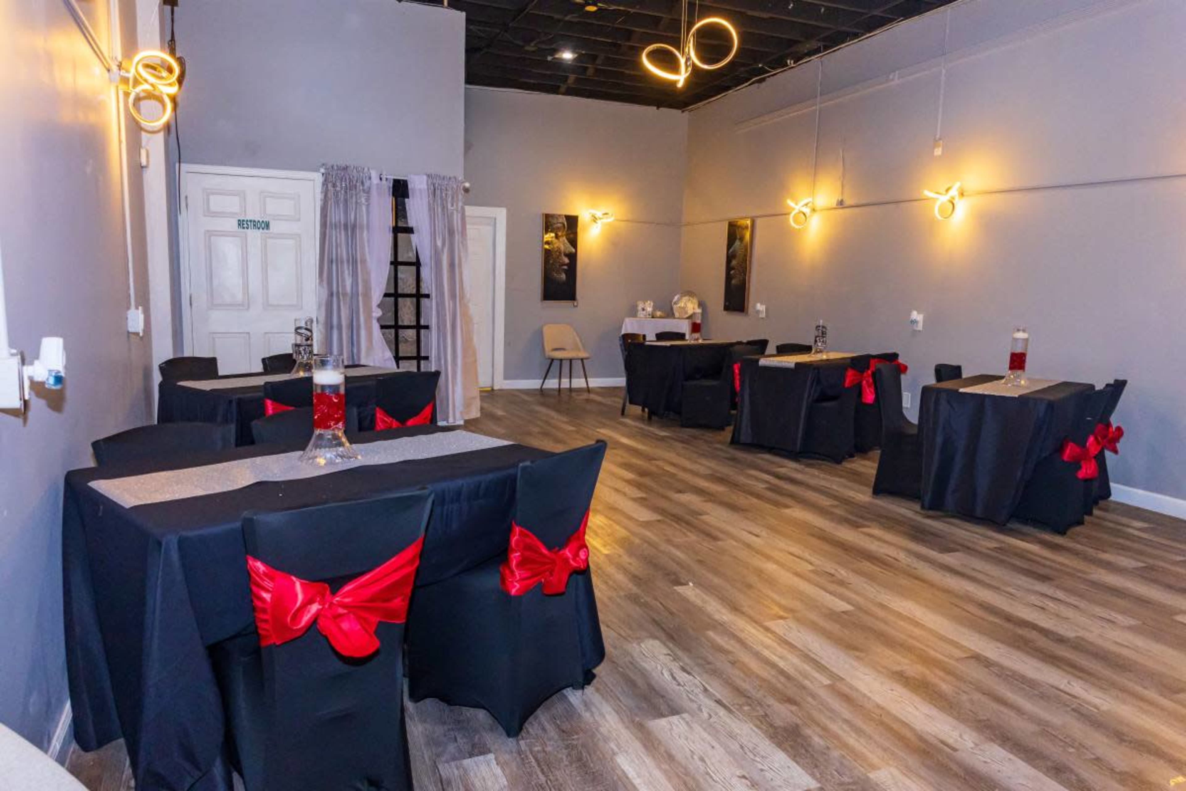The image shows a spacious event room featuring several tables covered with black tablecloths, each adorned with a red bow and set up for a gathering.