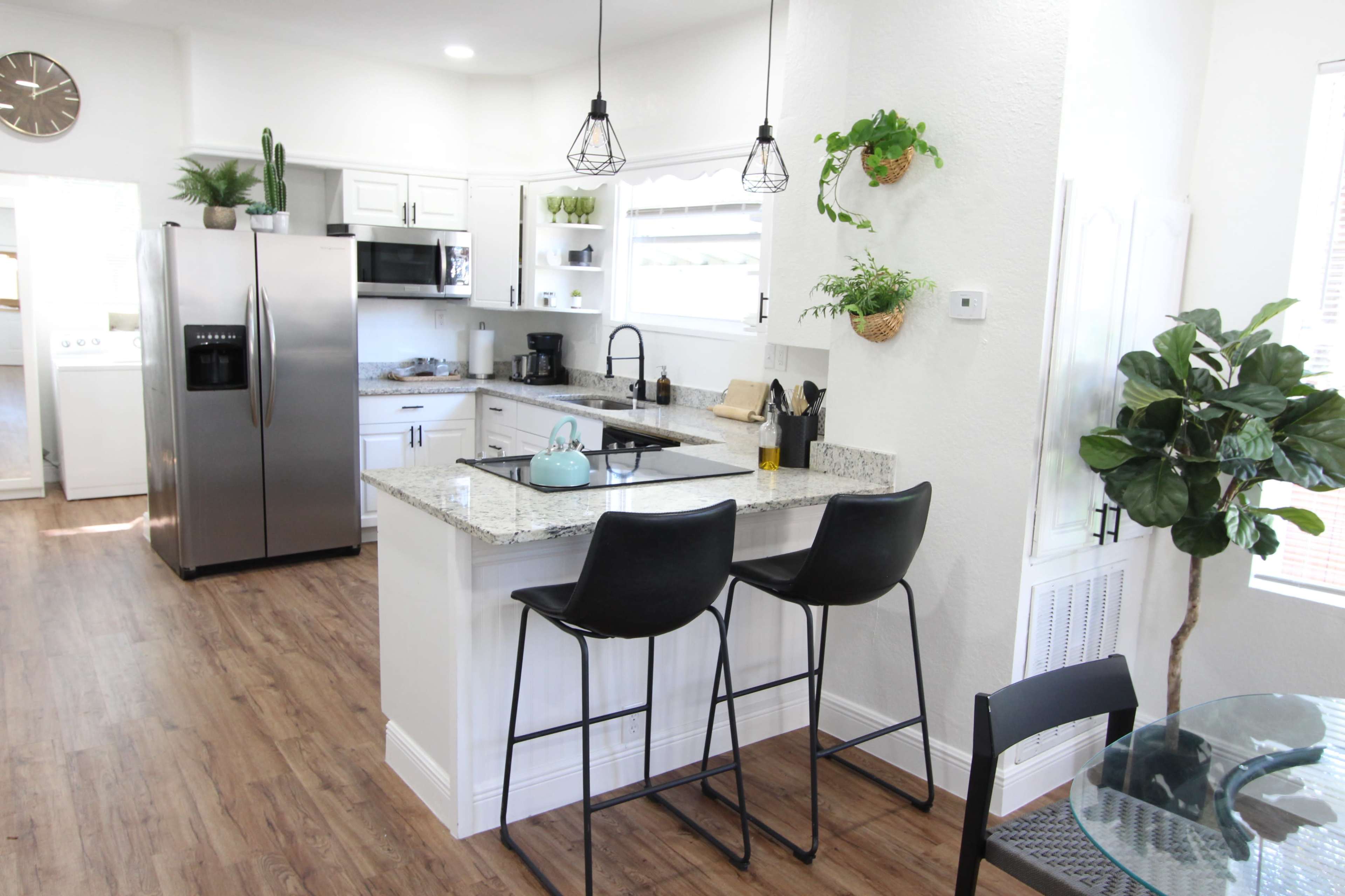 A modern kitchen features stainless steel appliances, granite countertops, and a small breakfast bar with two stools.