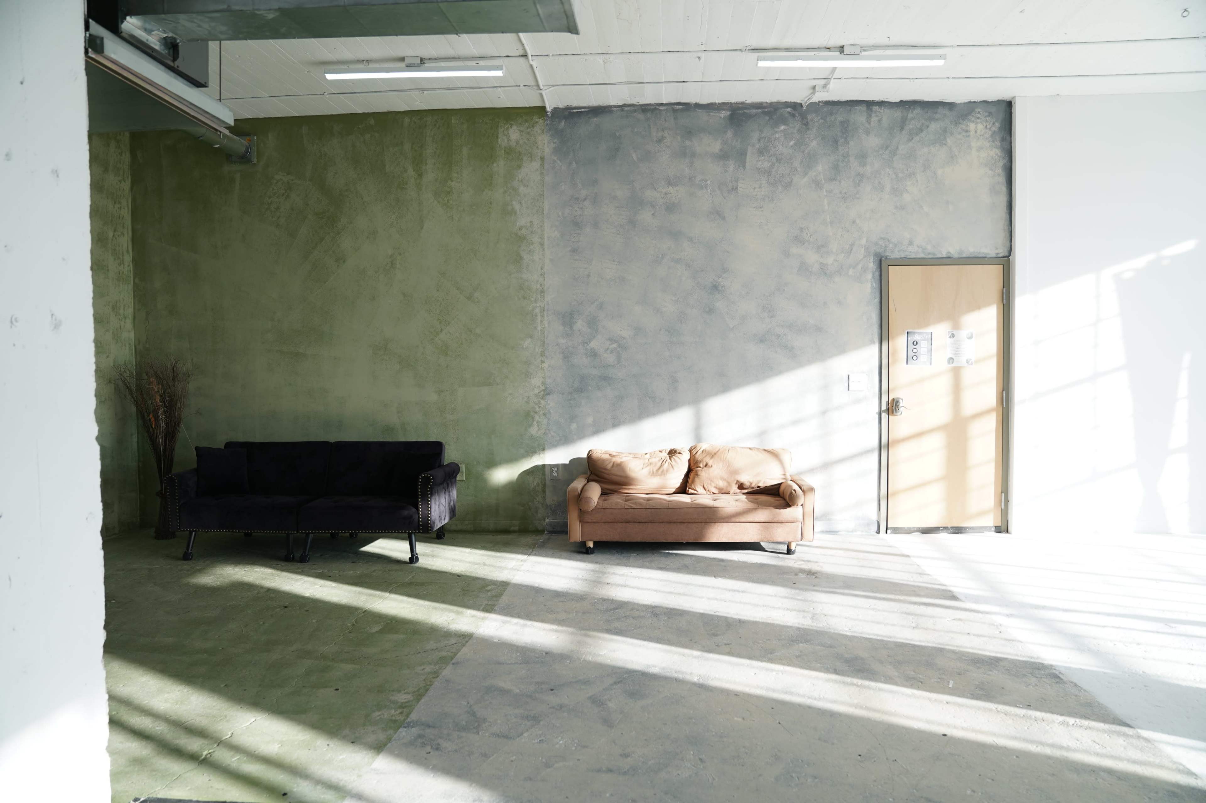 The image shows a well-lit room with two sofas, one black and one beige, against textured green and gray walls, and a door on the right.