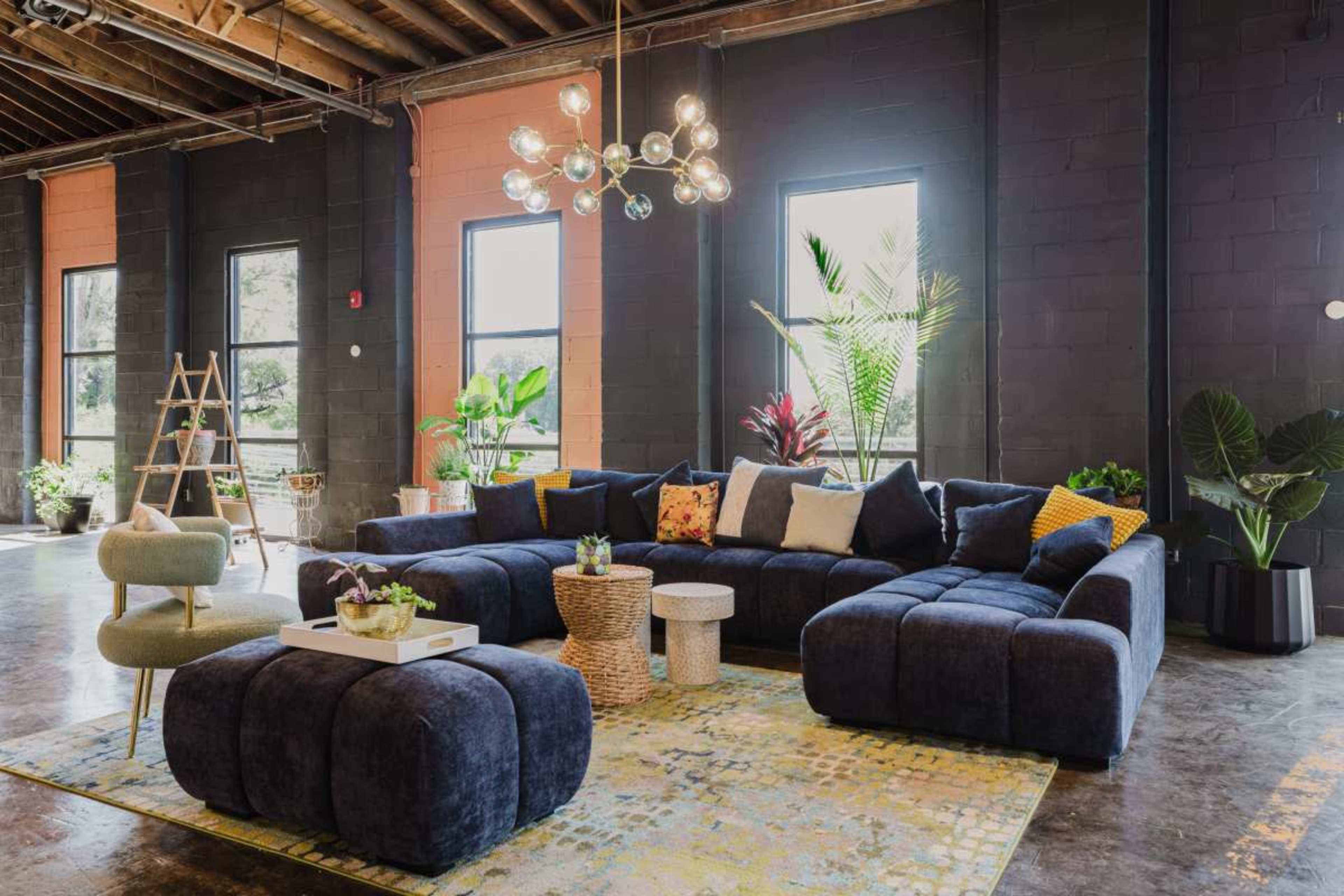The image shows a modern living room with a large sectional sofa, a coffee table, and plants, set against a backdrop of black walls and large windows.