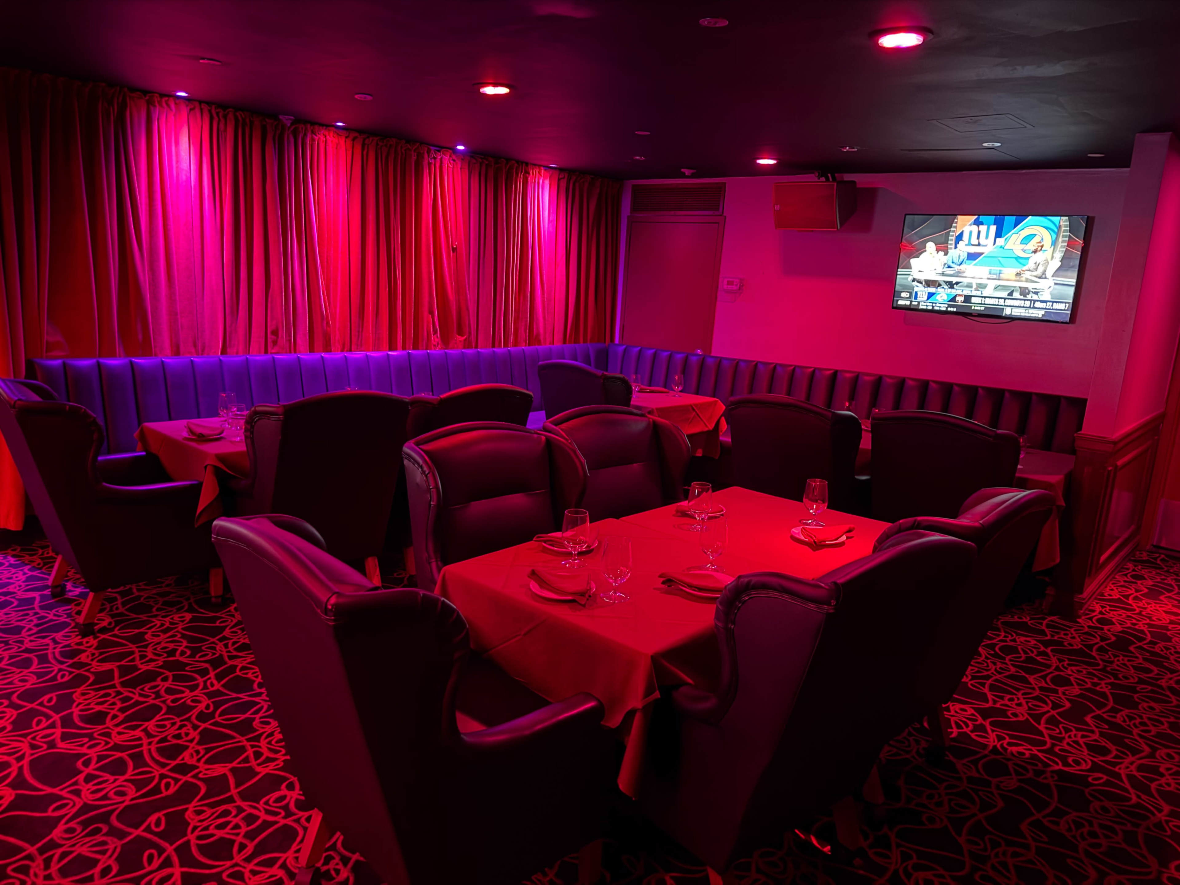 The image shows a dimly lit restaurant interior with red curtains, tables set with red tablecloths, and a television mounted on the wall.