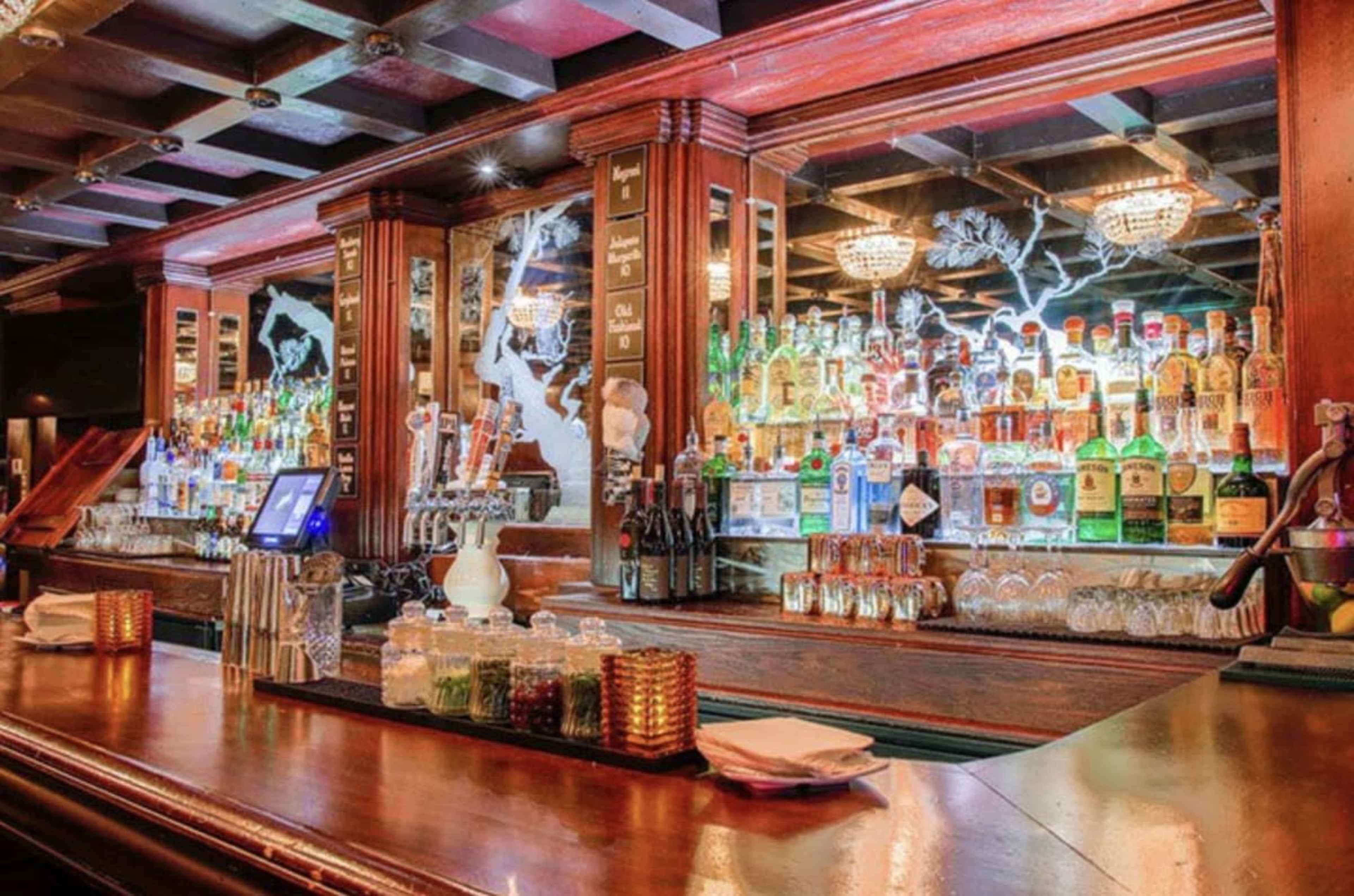 The image shows a well-stocked bar with an array of colorful bottles and glasses displayed behind the counter.