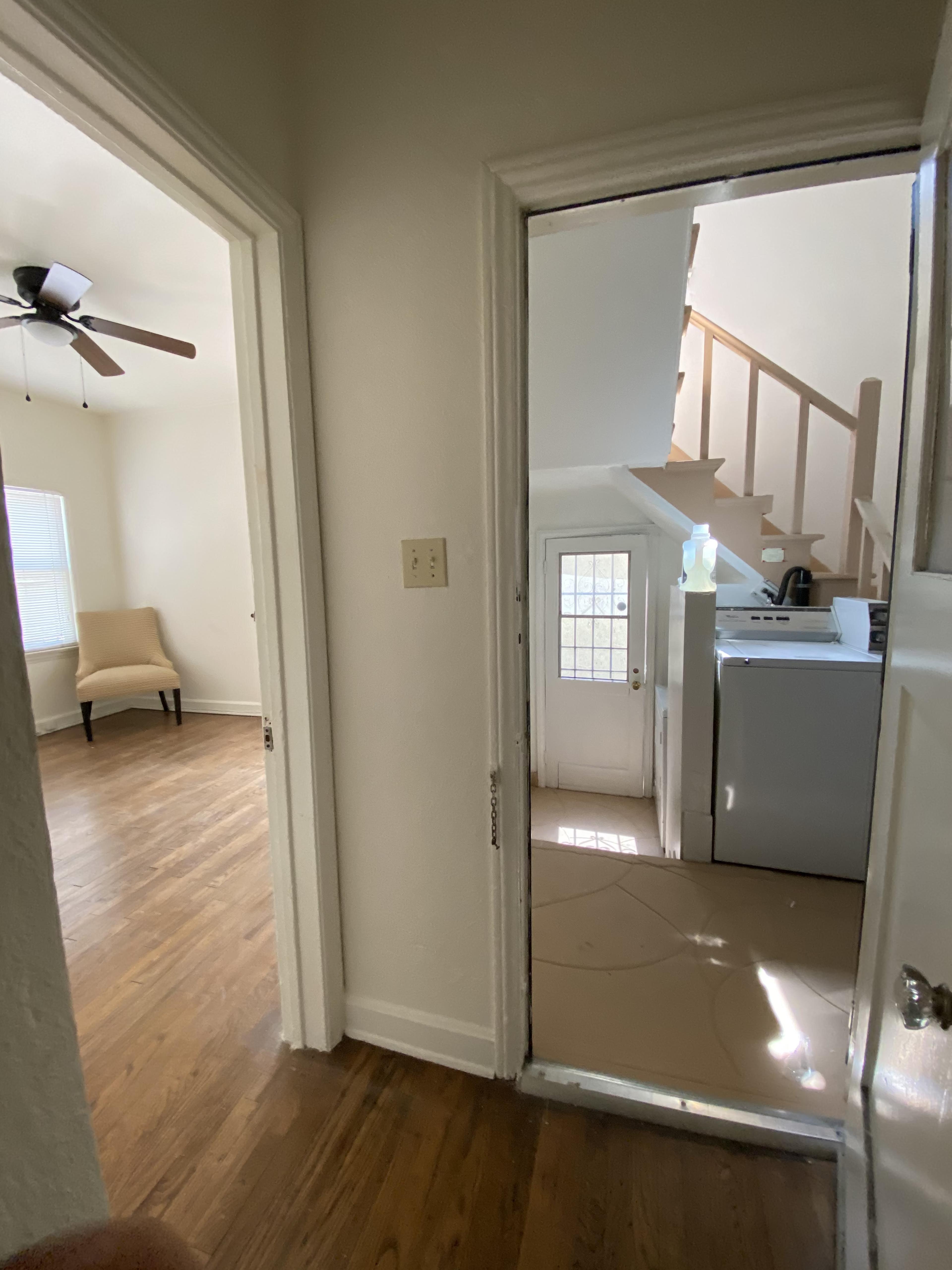 The image shows a hallway with doorways leading to a room on the left and a laundry area on the right, with stairs visible in the background.
