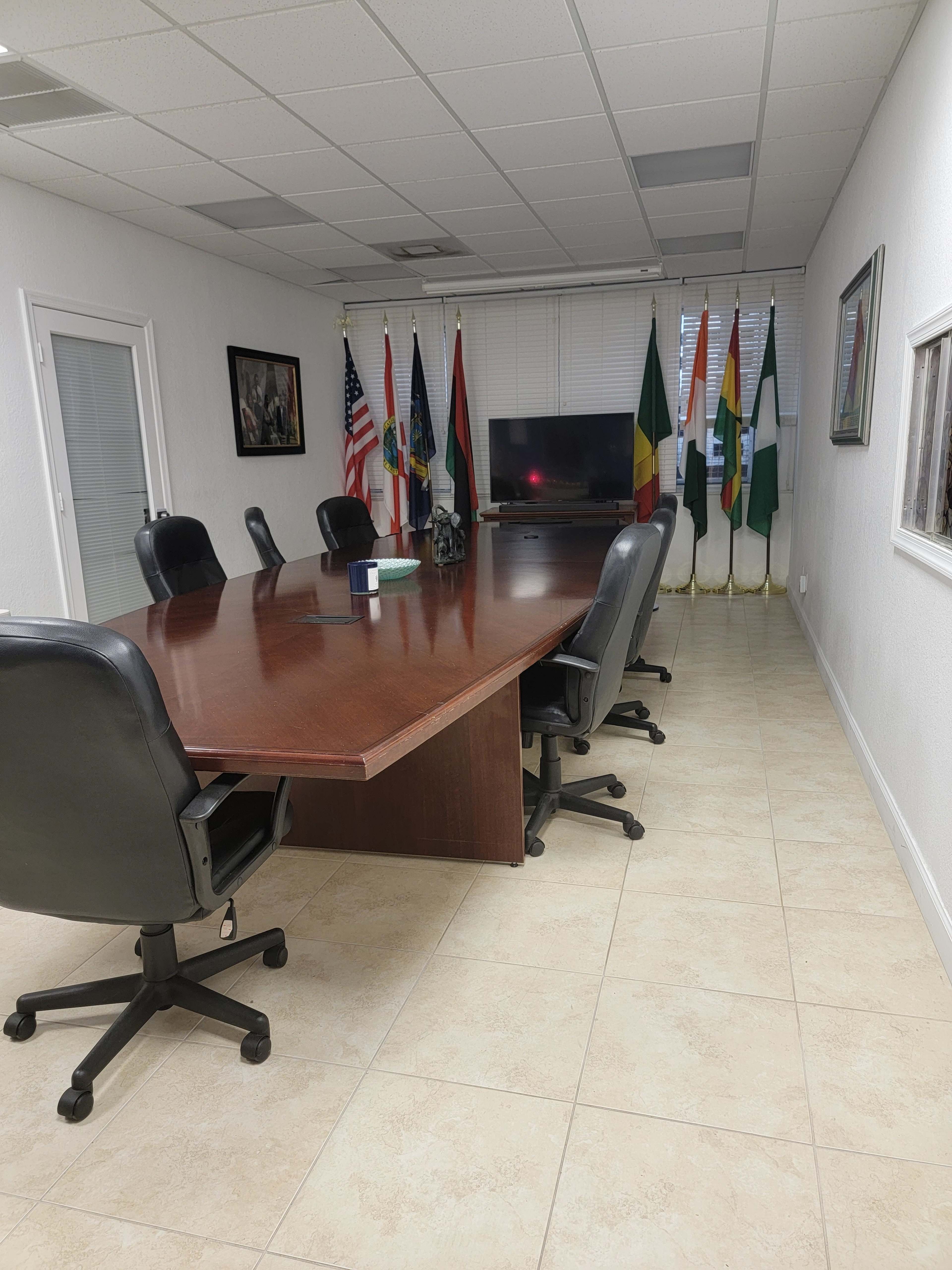 A large conference room features a wooden table surrounded by black leather chairs and various national flags displayed along the wall.