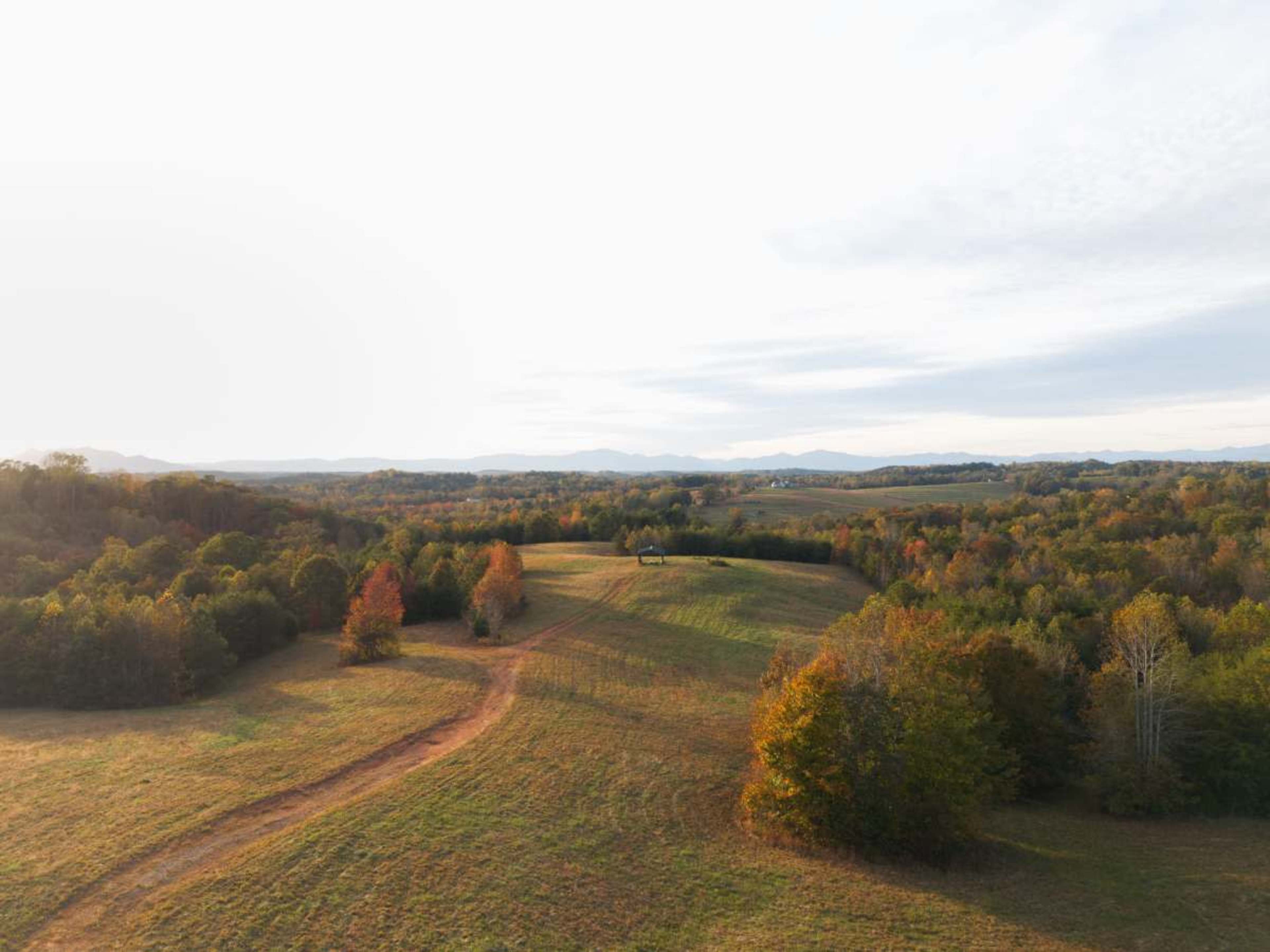 The image shows a panoramic view of rolling hills covered in autumn foliage, with a small structure visible in the distance.