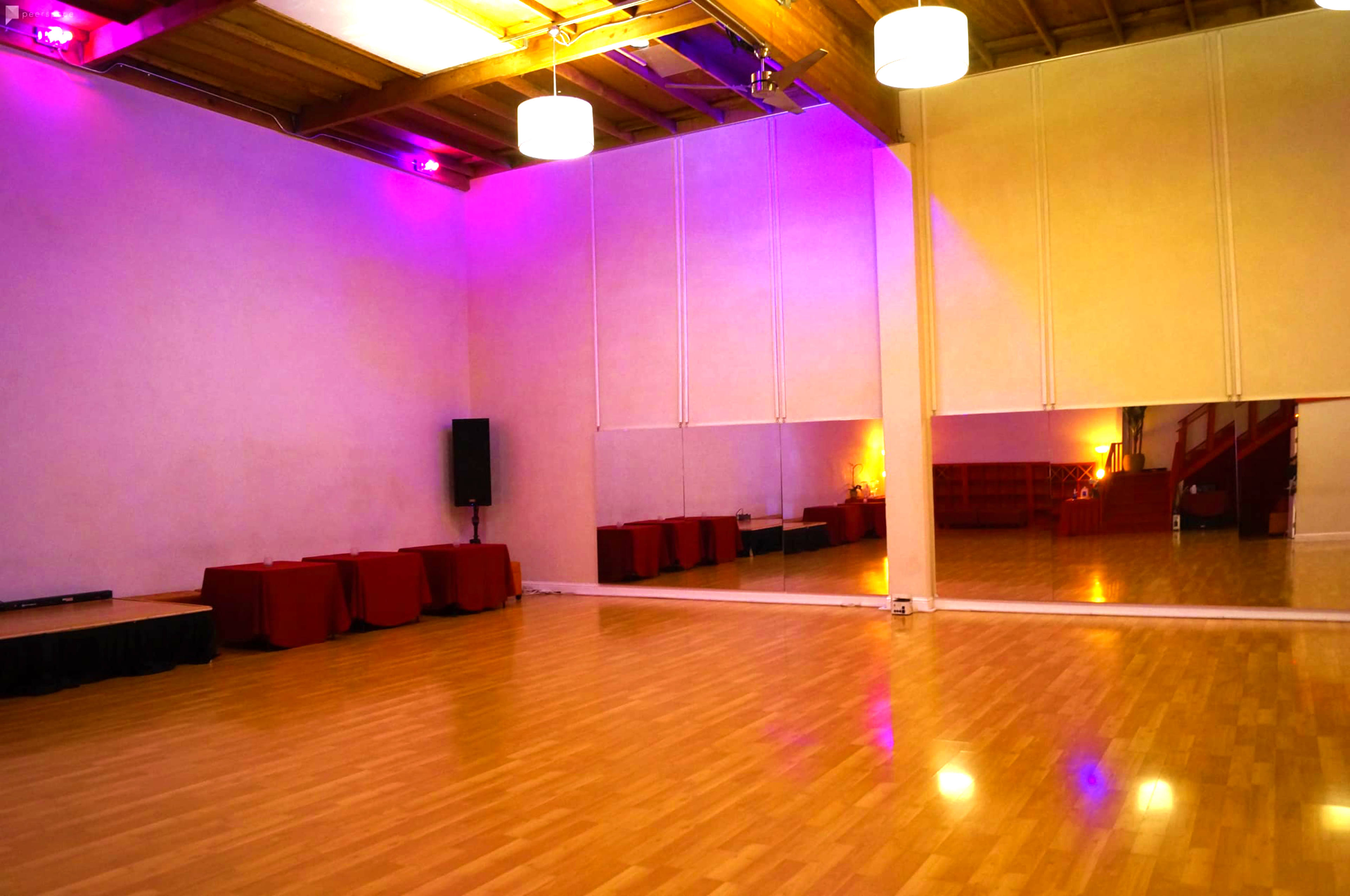 A spacious dance studio with wooden floors, purple lighting, and a large mirrored wall.