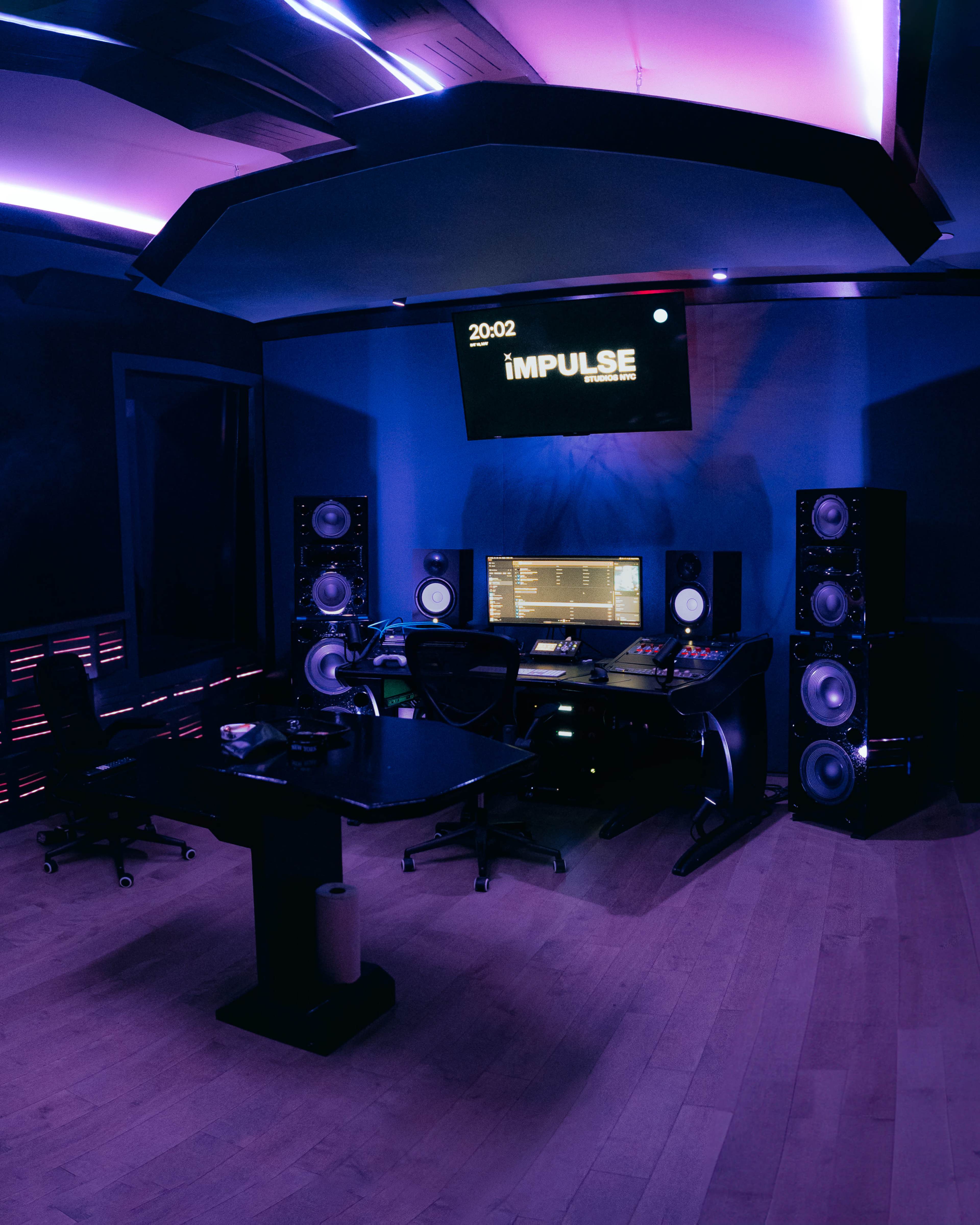 A modern music studio features a central mixing desk, large speakers, and ambient lighting in a dark blue environment.