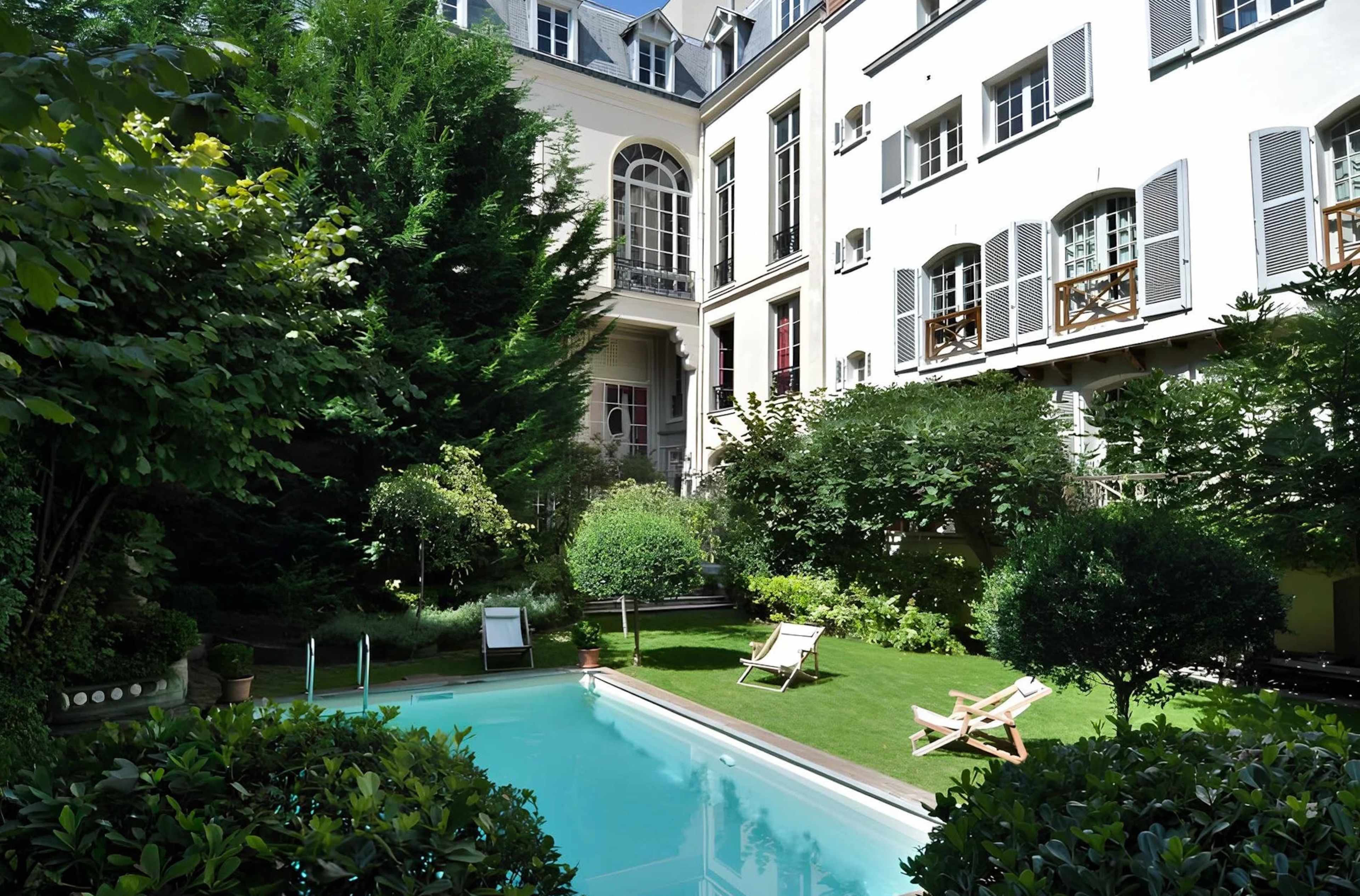 The image shows a tranquil garden with a swimming pool surrounded by lush greenery and a multi-story building in the background.
