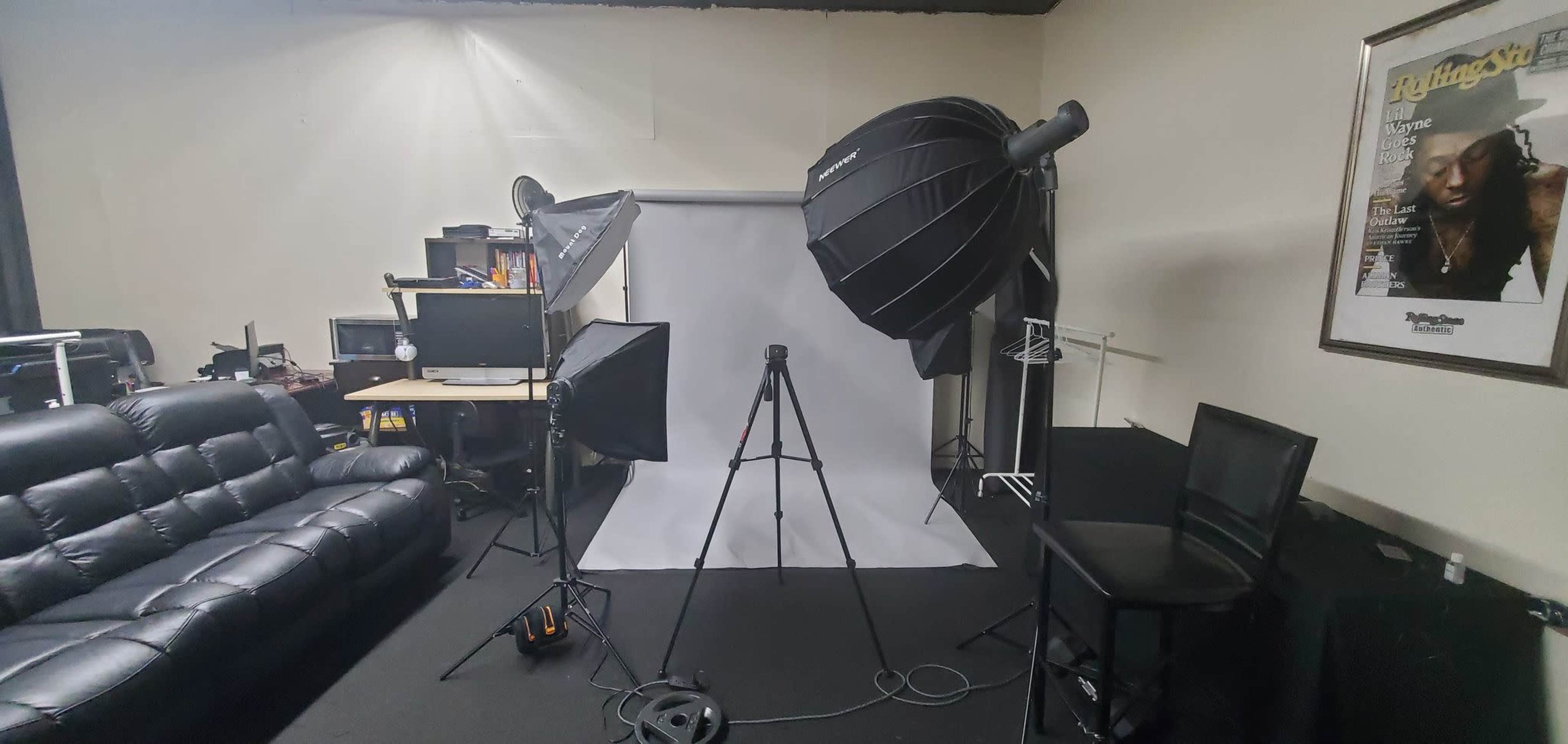 A photography studio featuring lighting equipment, a backdrop, a tripod, and a seating area.