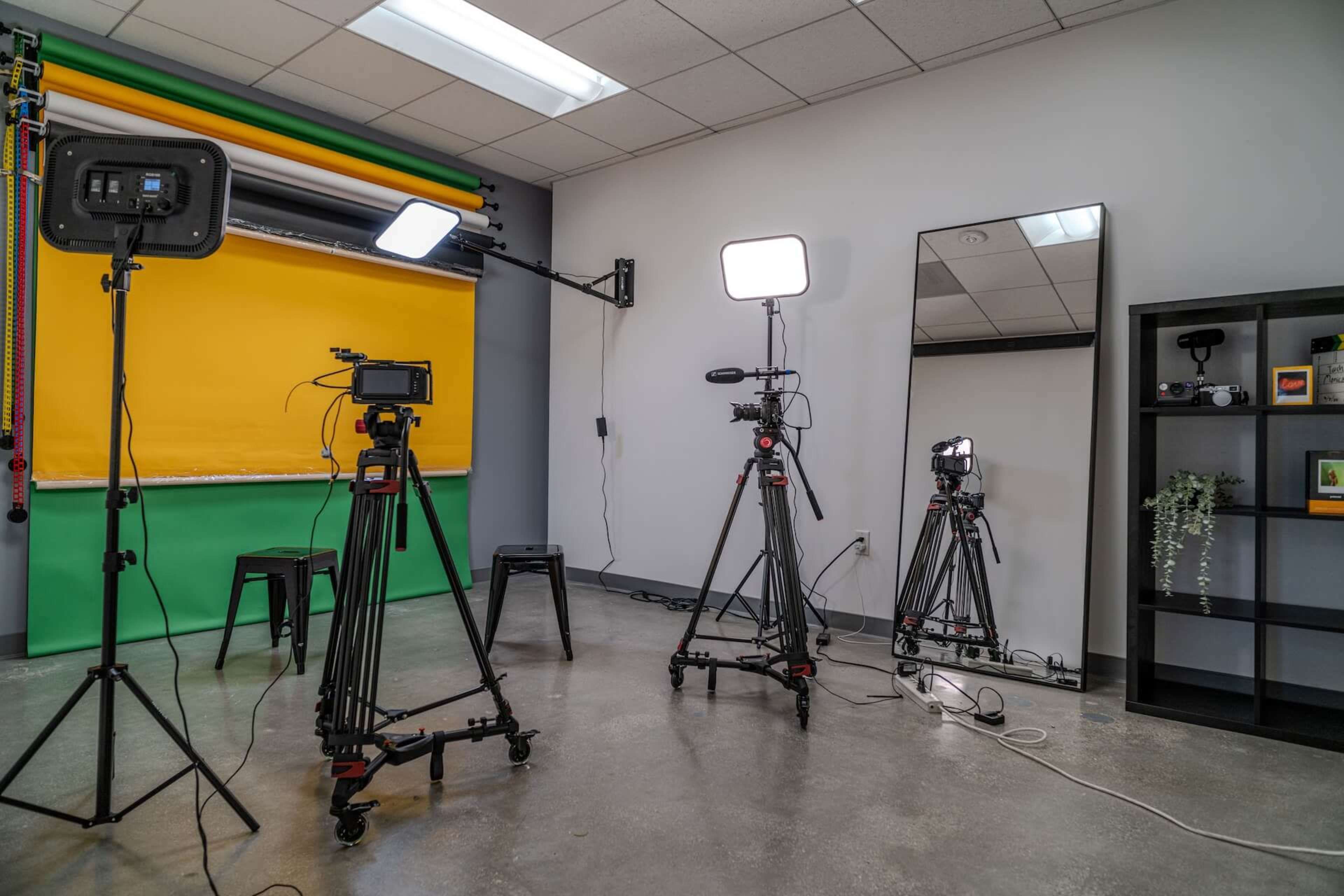 A photography studio is set up with multiple tripods, lighting equipment, a large mirror, and a colorful backdrop.