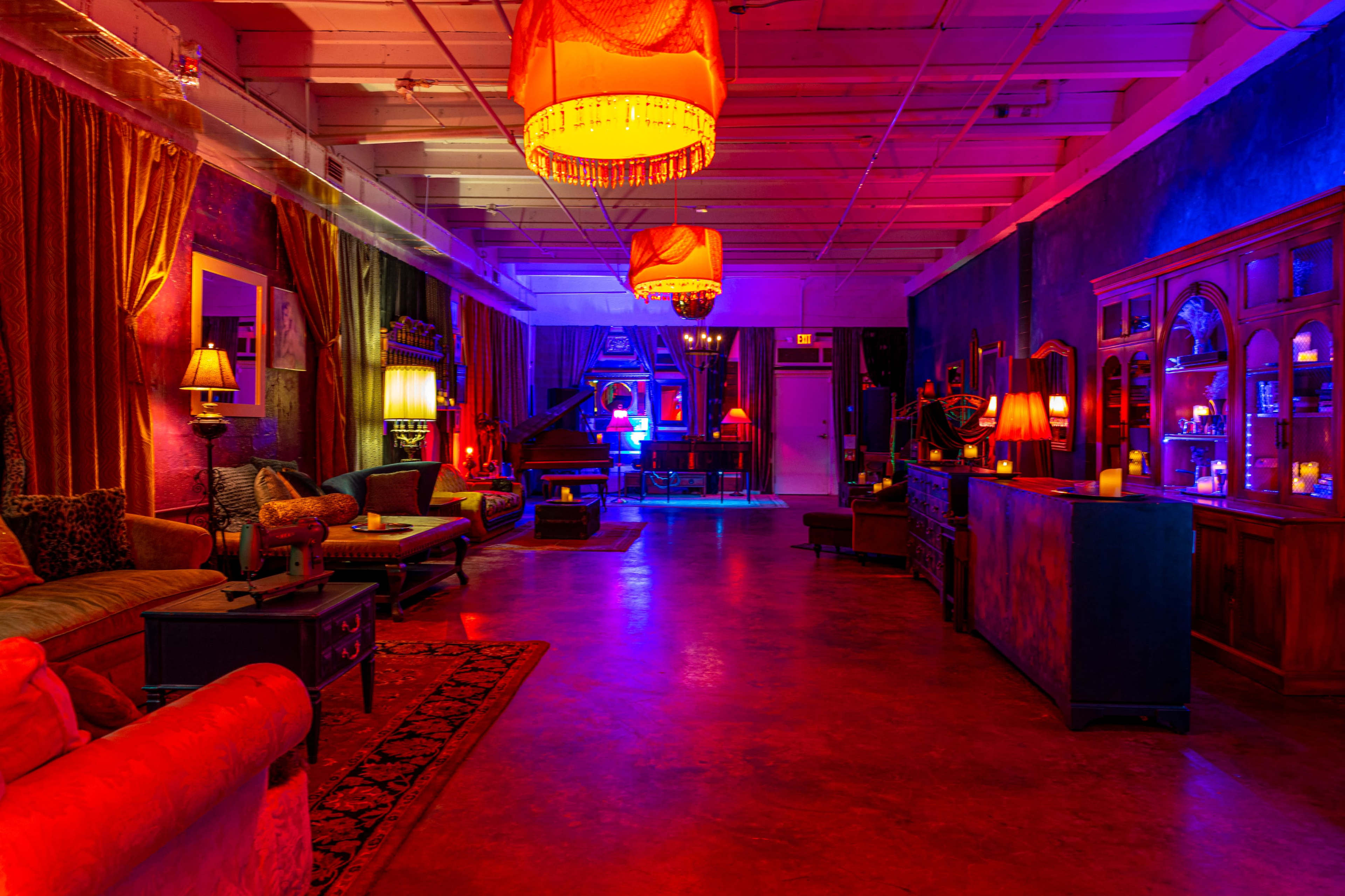 The scene features a spacious room with colorful lighting, a grand piano, elegant furnishings, and a bar area, creating a vibrant and inviting atmosphere.