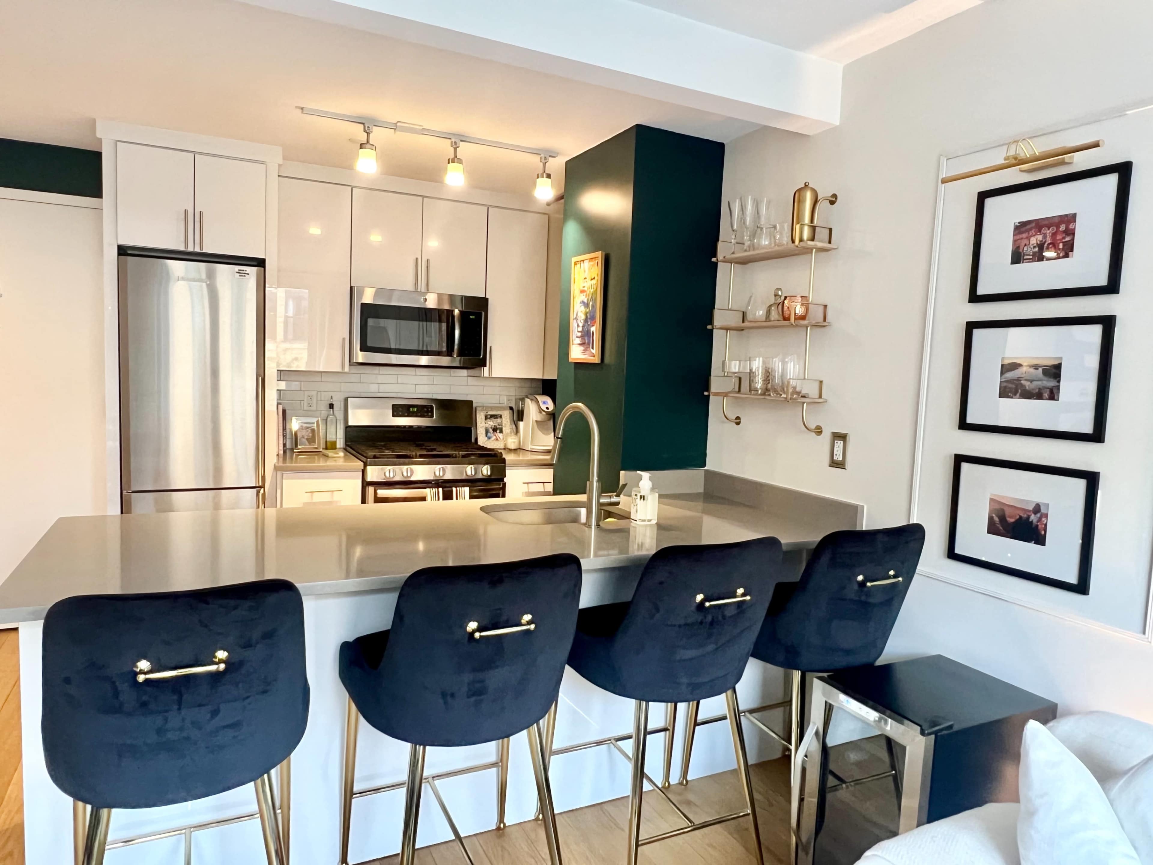 A modern kitchen with a gray countertop, stainless steel appliances, and four black bar stools along a breakfast bar.