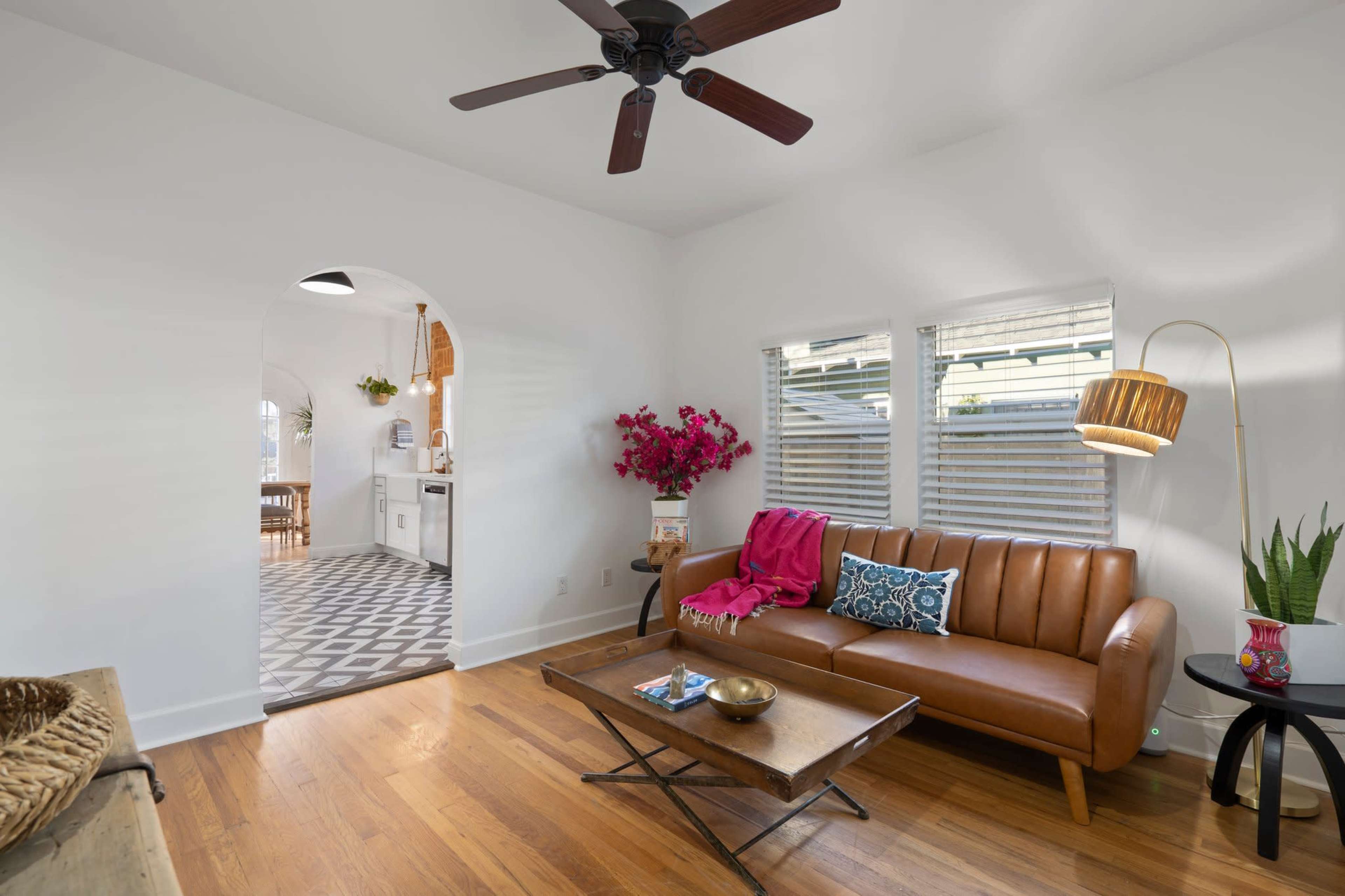 A modern living room features a brown leather sofa, a wooden coffee table, and an archway leading to a kitchen with a patterned floor.